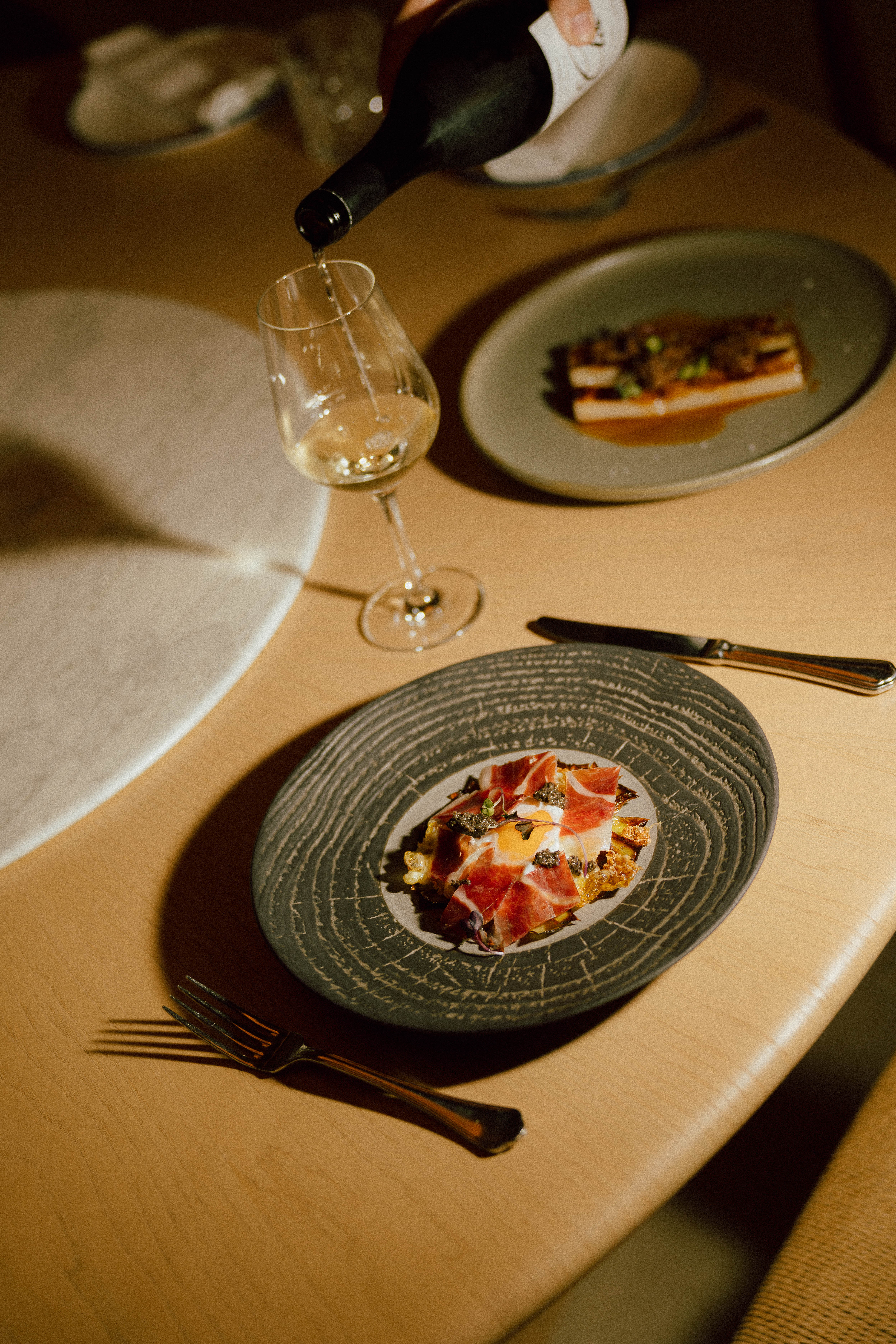 Pouring white wine; plate of Iberian ham, fried egg, and truffle.