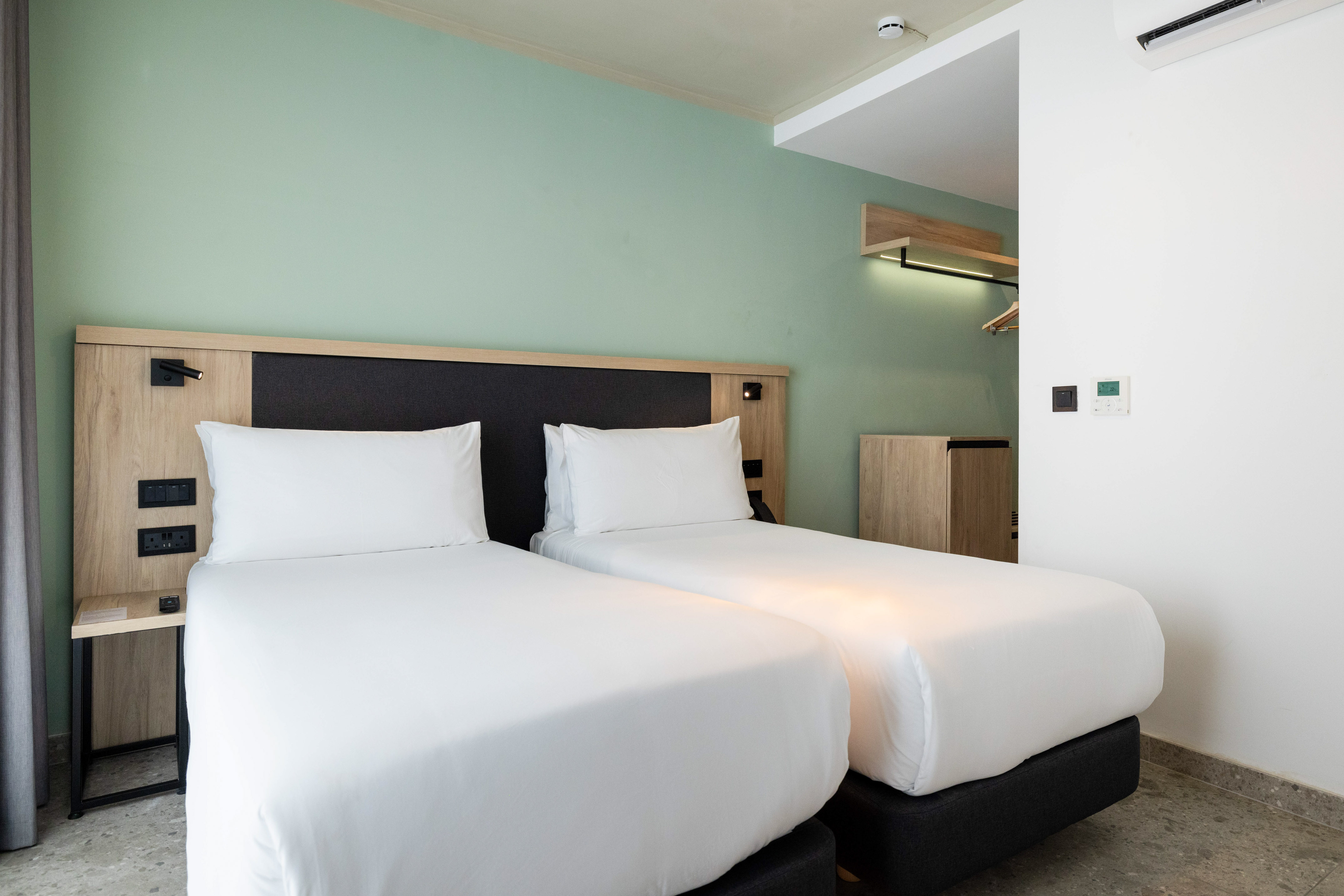 Modern hotel room with twin beds, white bedding, and green accent wall.