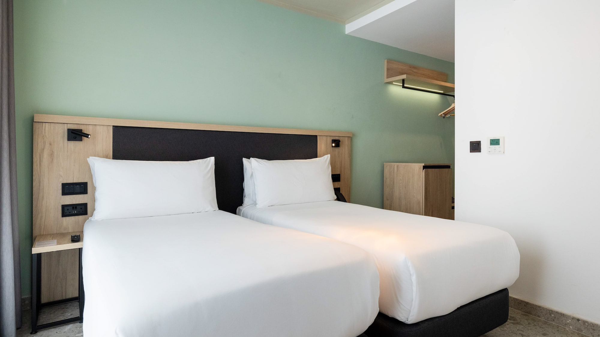 Modern hotel room with twin beds, white bedding, and green accent wall.