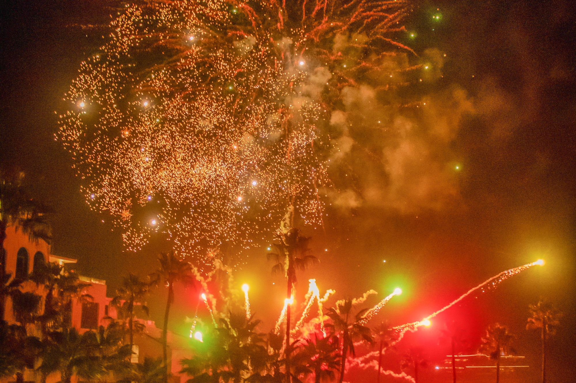 Colorful fireworks over a resort pool and palm trees at night.
