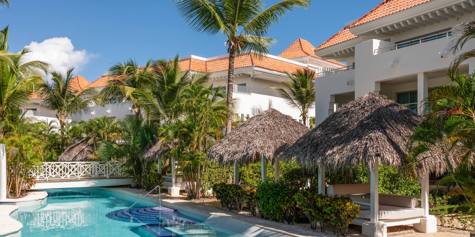 a pool with palm trees and a building with a thatched roof