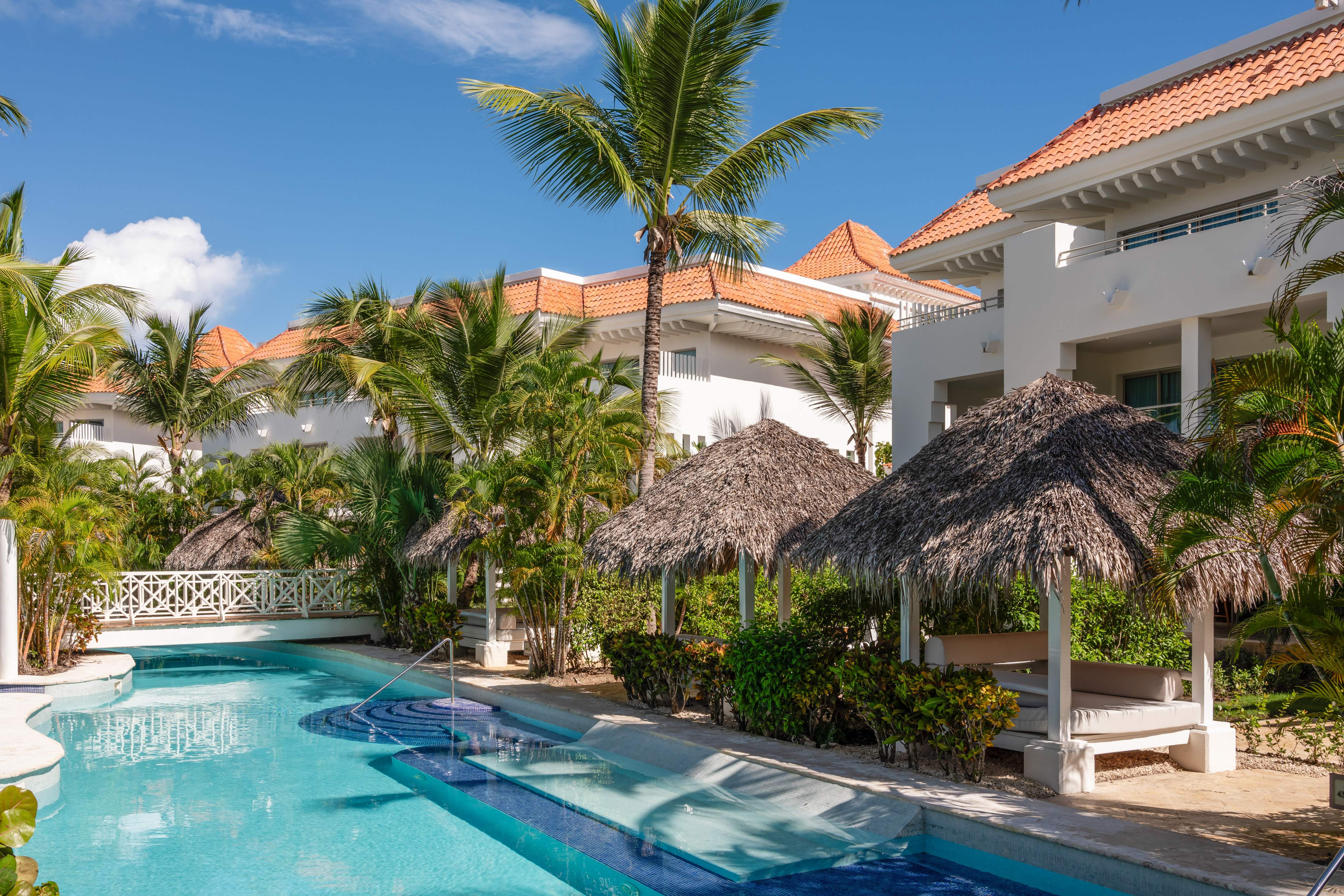 a pool with palm trees and a building with a thatched roof