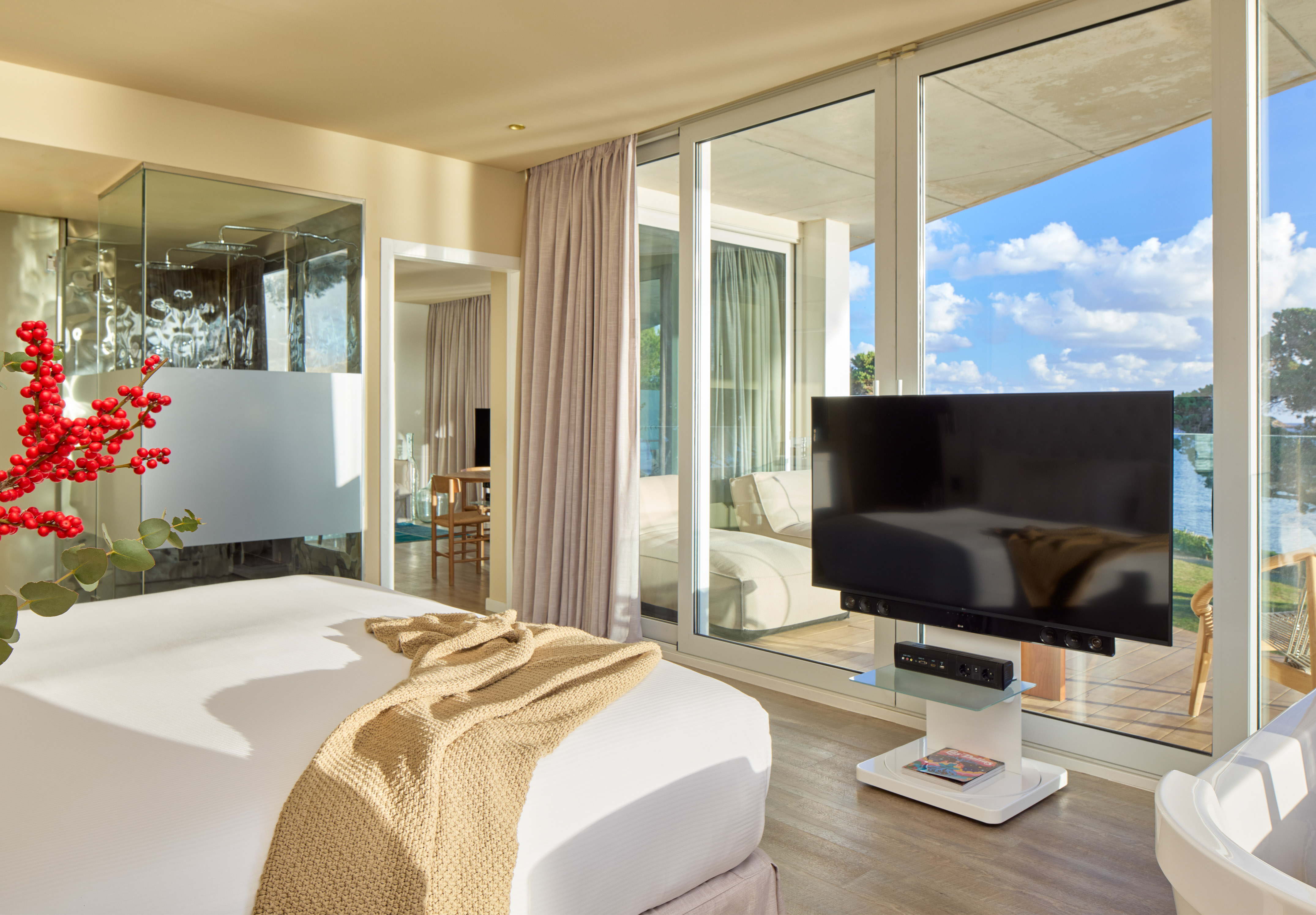 Modern hotel bedroom with waterfront view, TV, sliding doors, and glass shower.