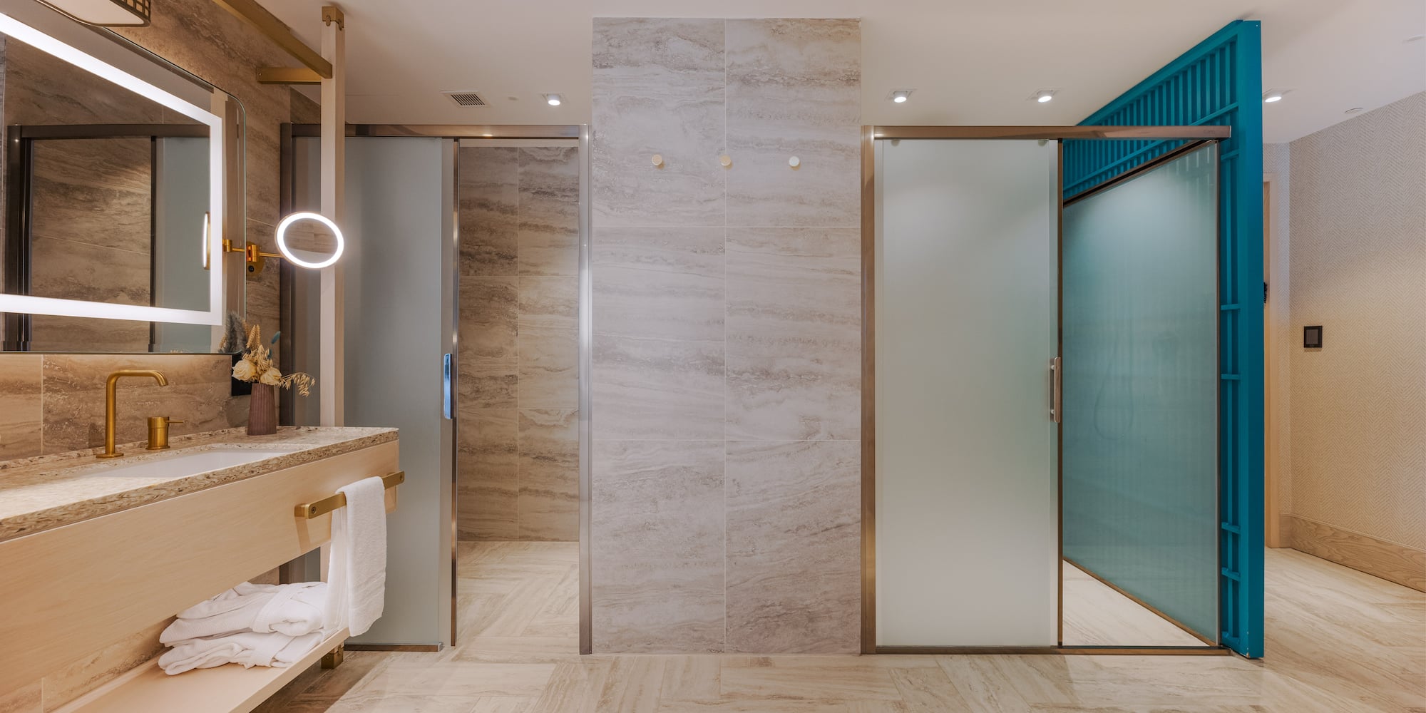 Modern bathroom with gold fixtures, LED mirror, and frosted glass doors.