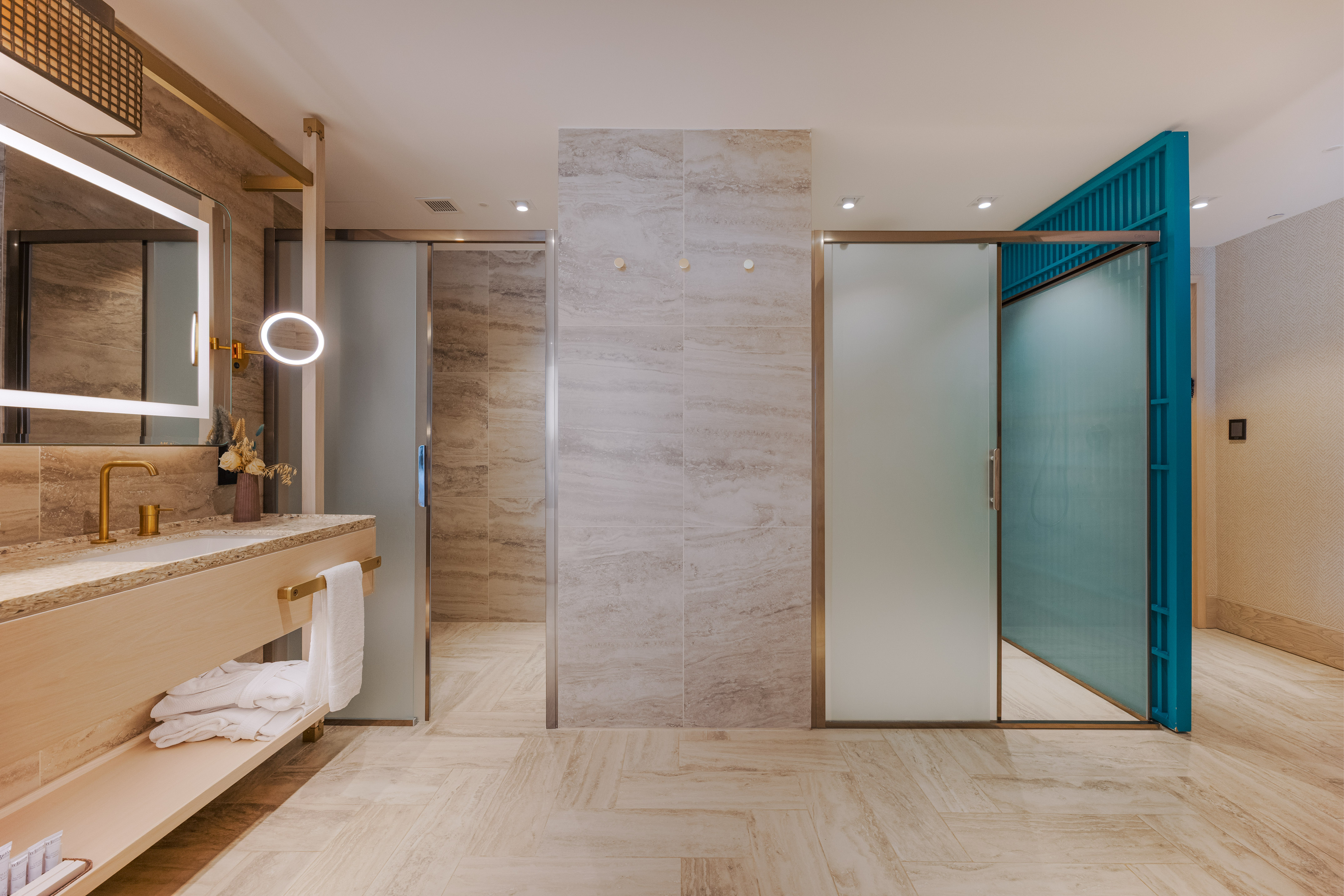 Modern bathroom with gold fixtures, LED mirror, and frosted glass doors.