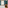 Modern hotel room with white bed, arched window, teal curtains, wooden table.