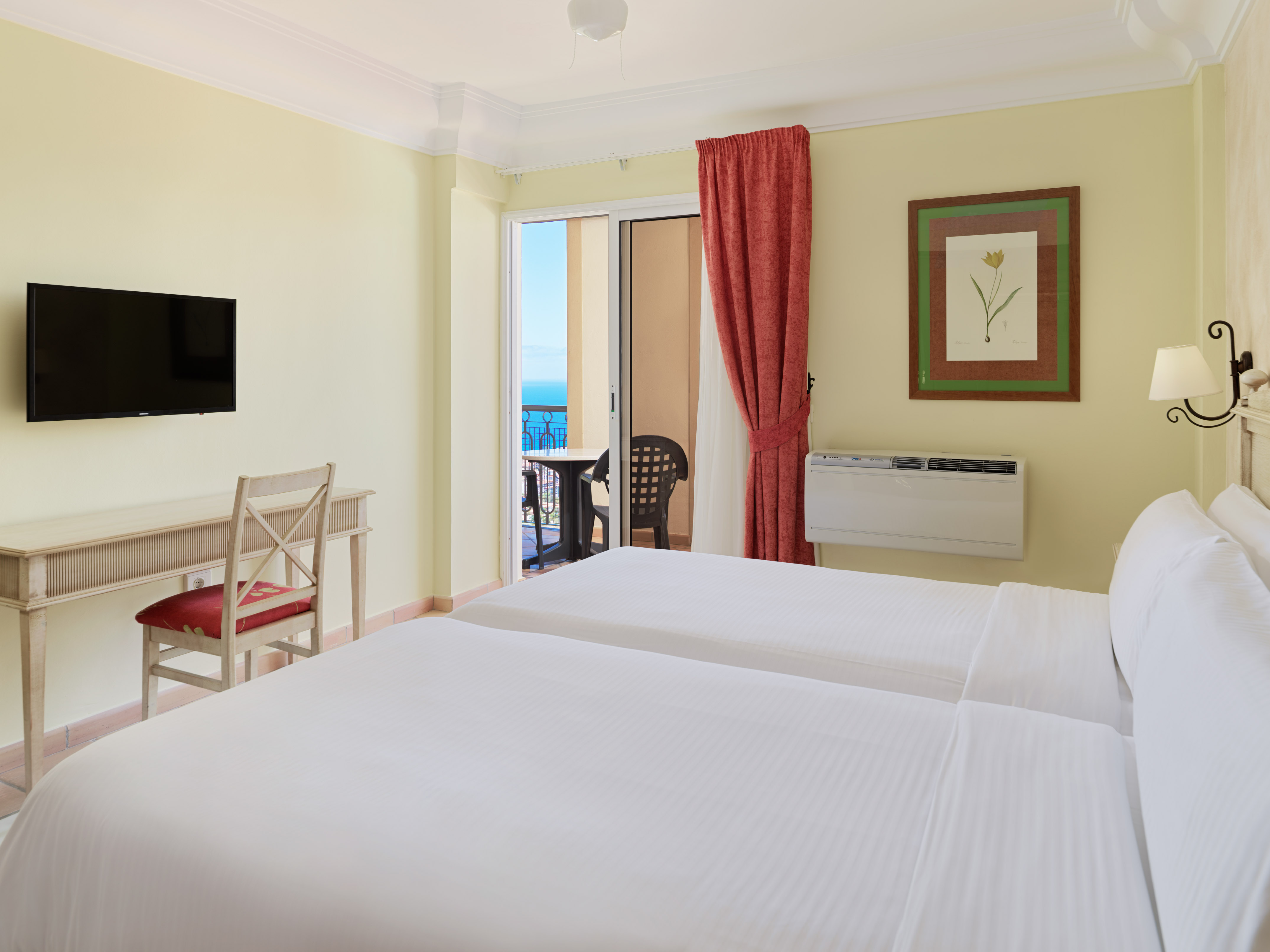 Hotel room with twin beds, desk, TV, and a balcony with an ocean view.