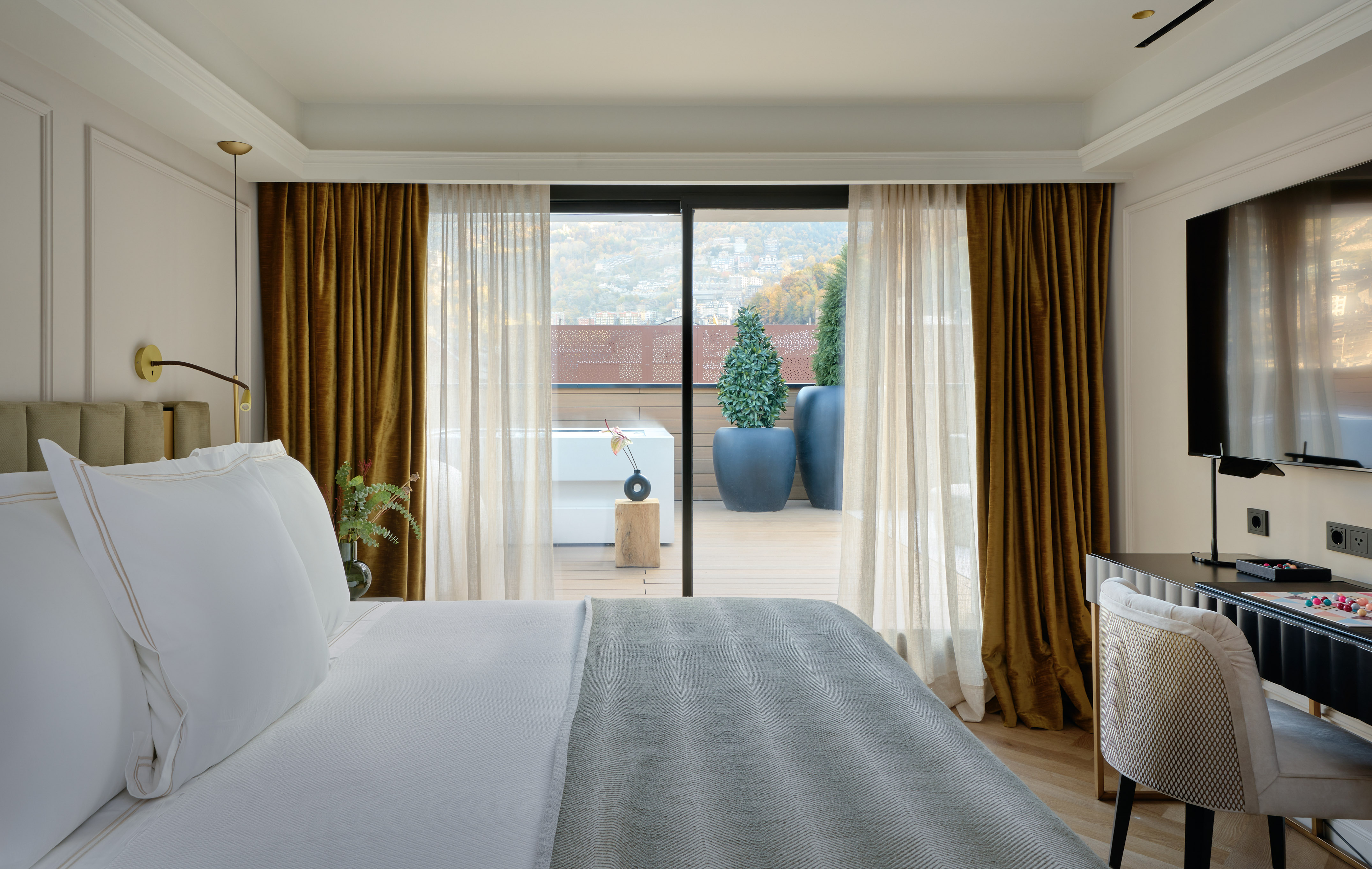 Modern hotel room with balcony, mountain view, and outdoor hot tub.