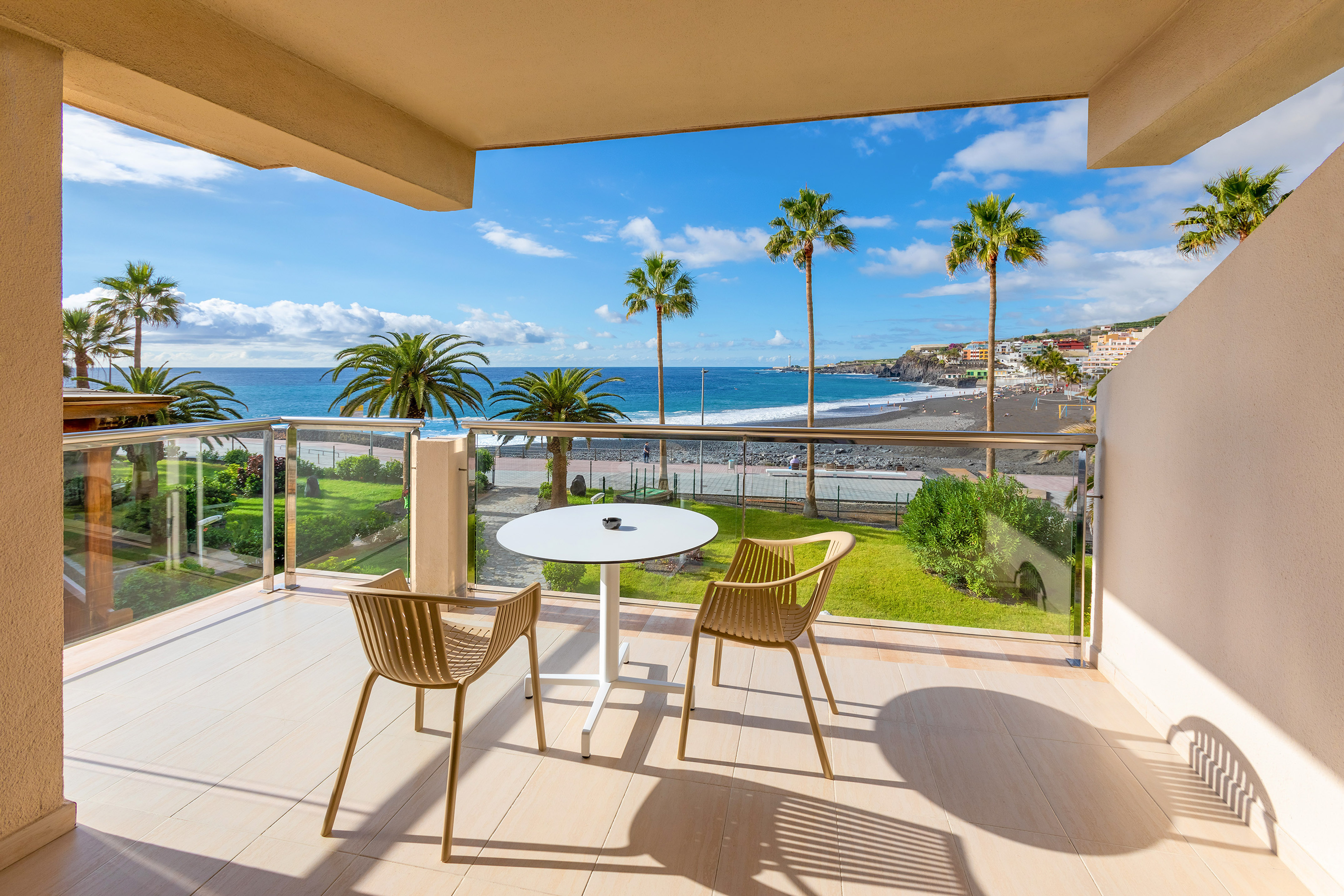 Balcony with ocean, palm trees, black sand beach, and resort town view.