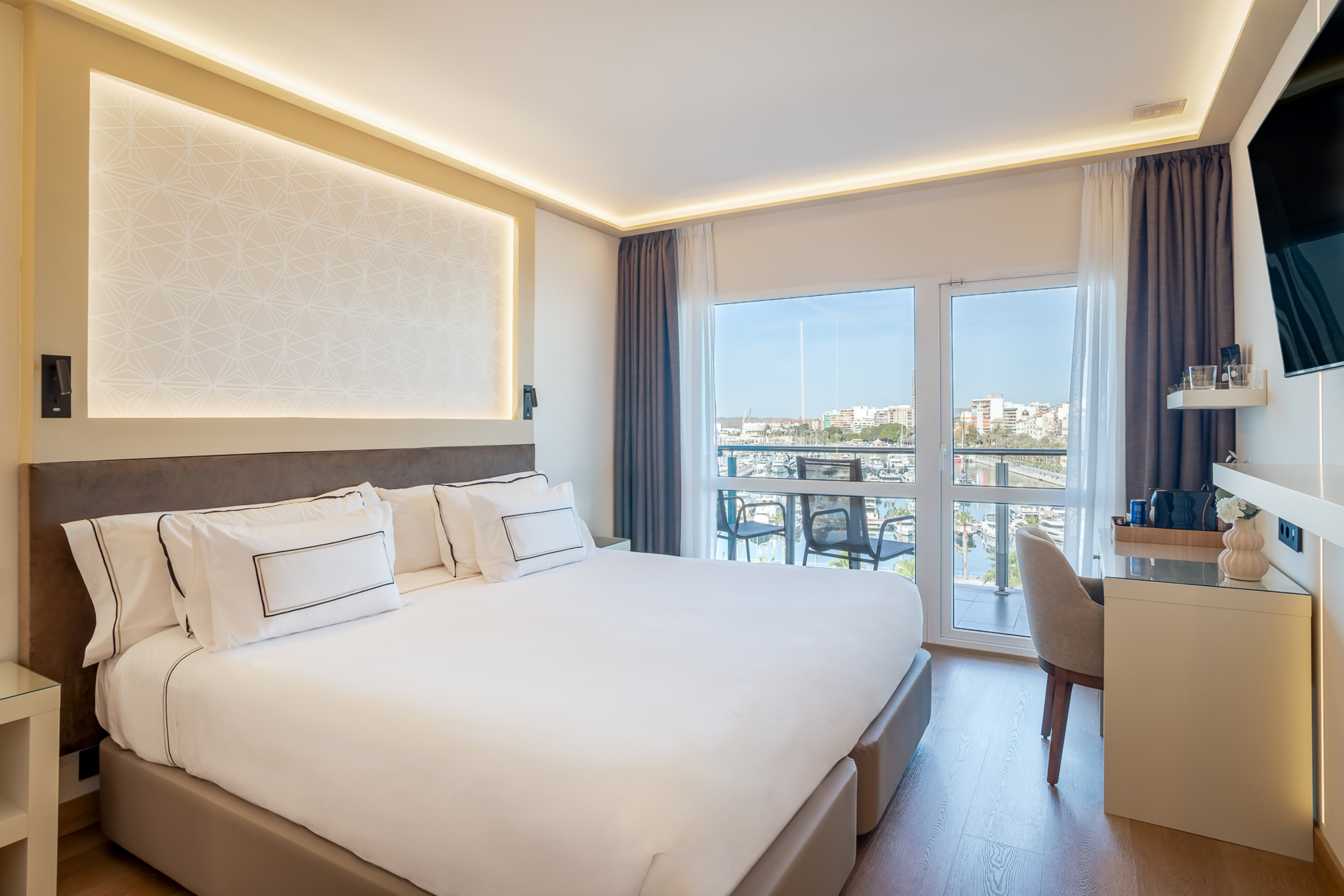 Modern hotel bedroom with king bed, balcony, and marina view.