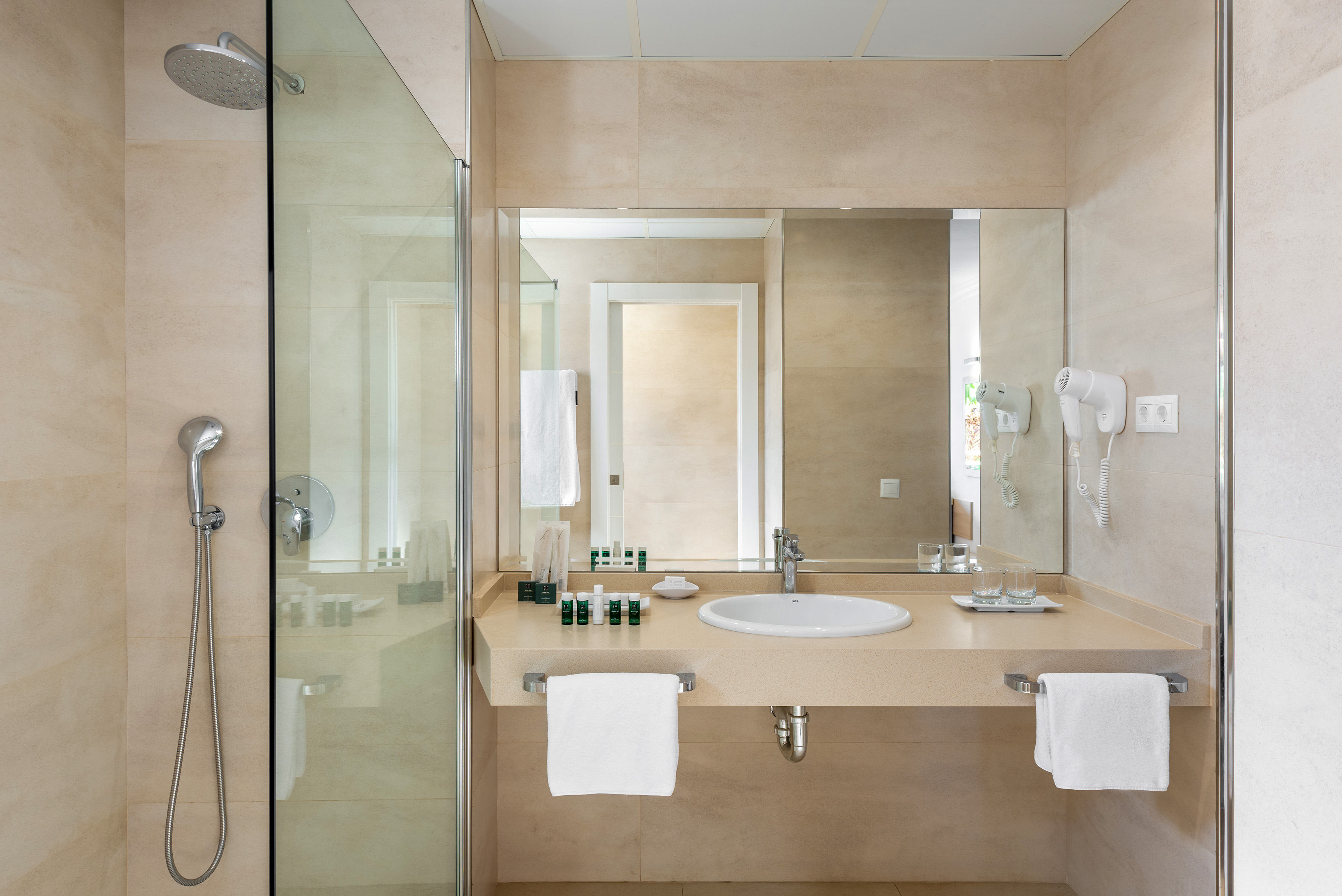 Hotel bathroom with modern walk-in shower, vanity, sink, and mirror.