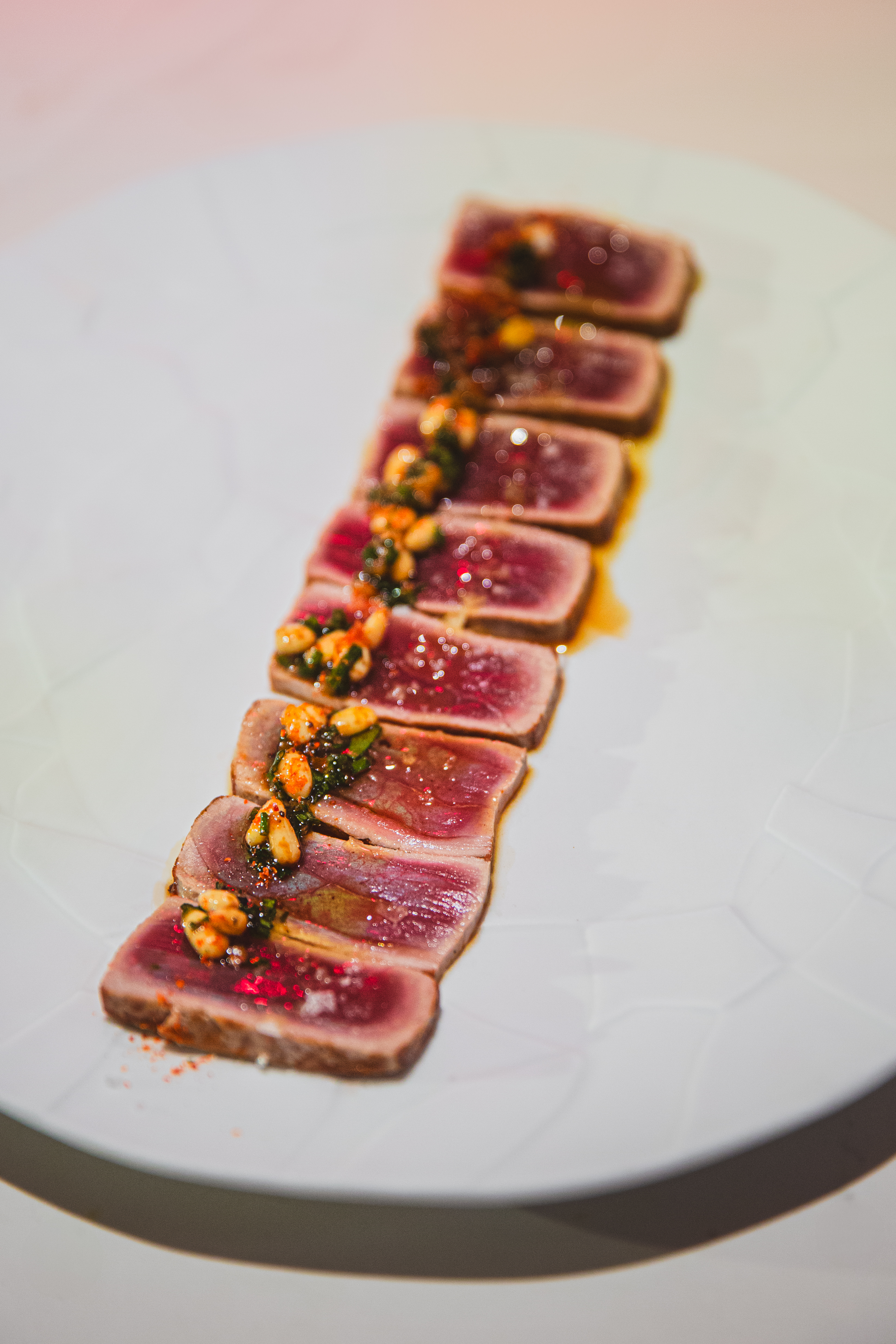 Seared tuna tataki slices topped with herb sauce, pine nuts, and red spices.