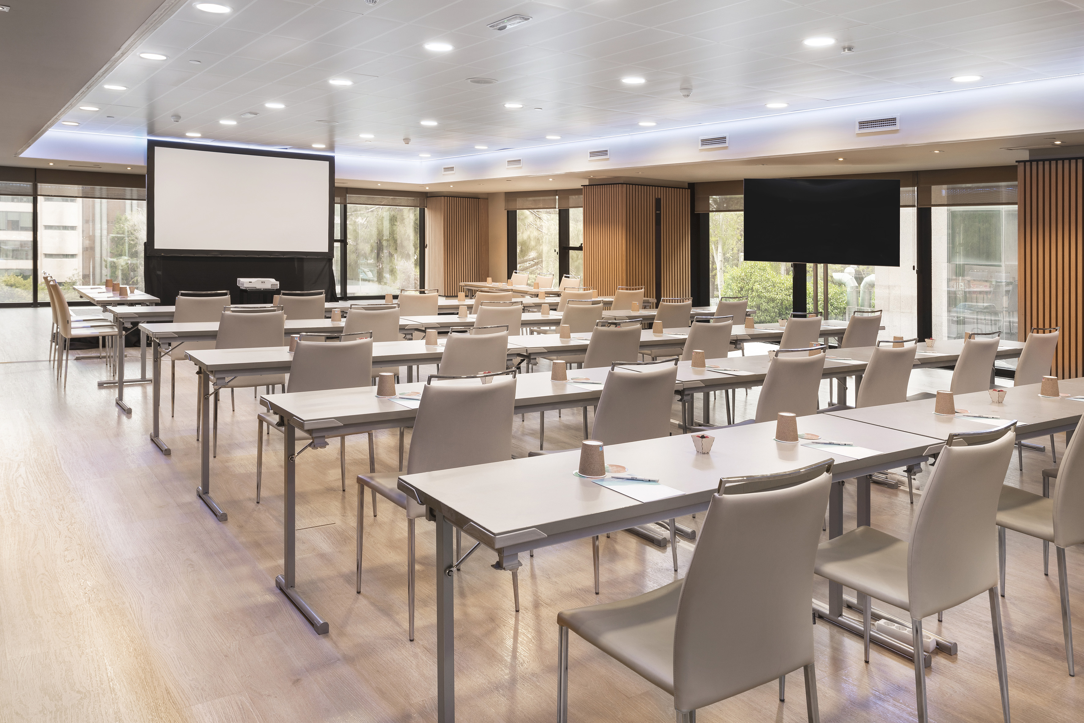 Modern meeting room with classroom setup, large projector screen, and TV.