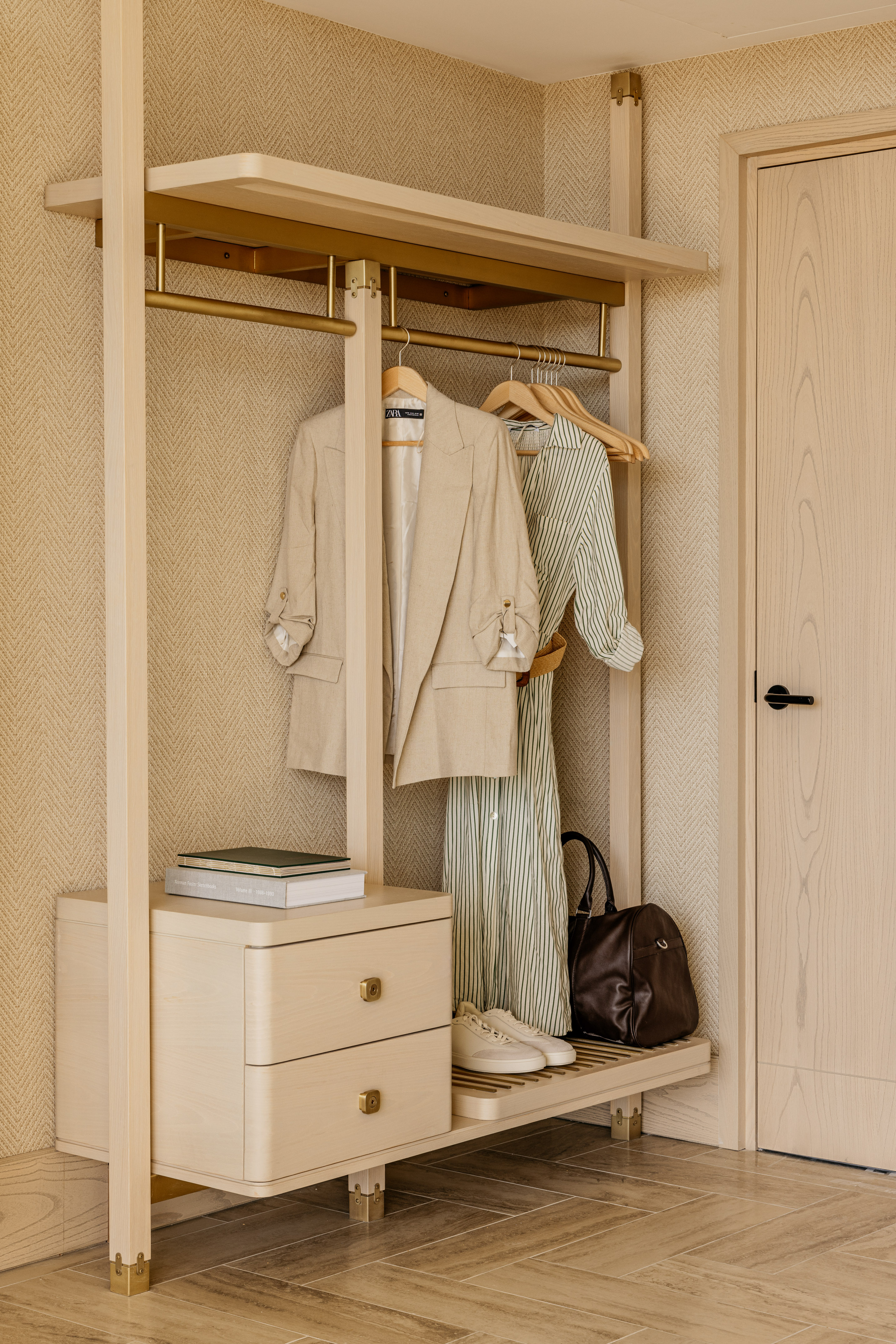 Open light wood wardrobe with hanging clothes, books, shoes, gold details.