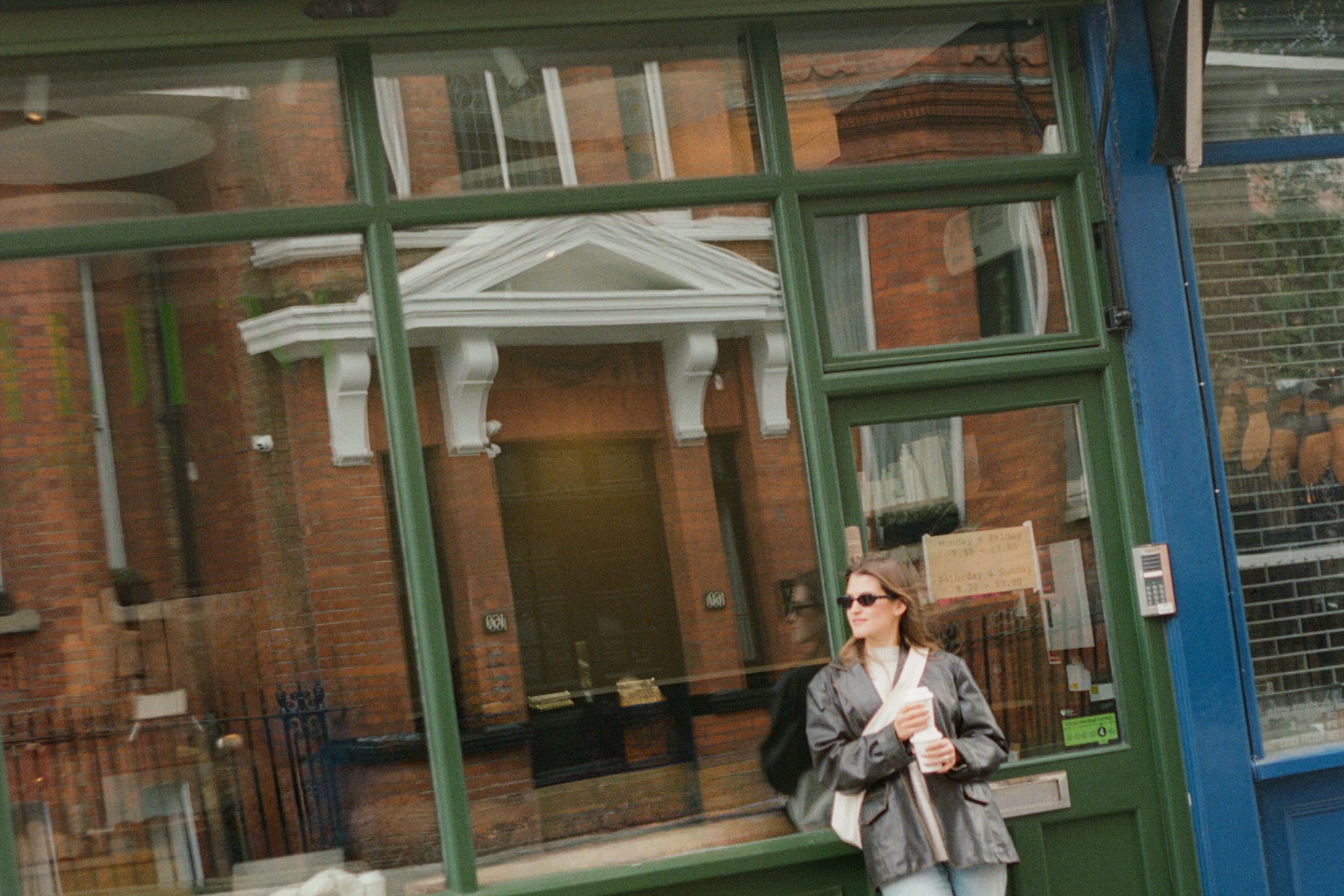 Mujer con café apoyada en el escaparate de HJEM South Kensington.