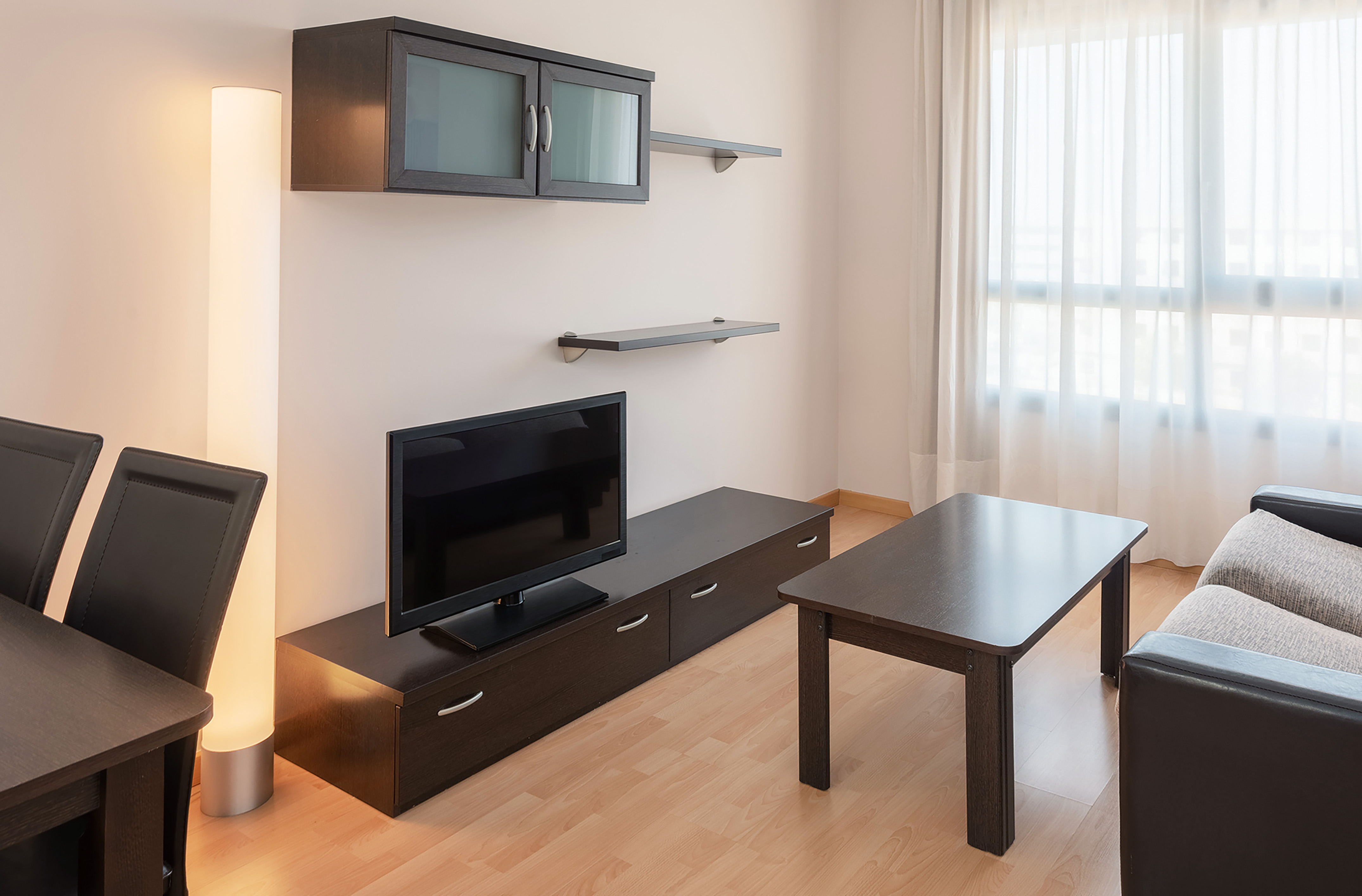 Modern apartment living room with TV, dark wood furniture, and bright window.