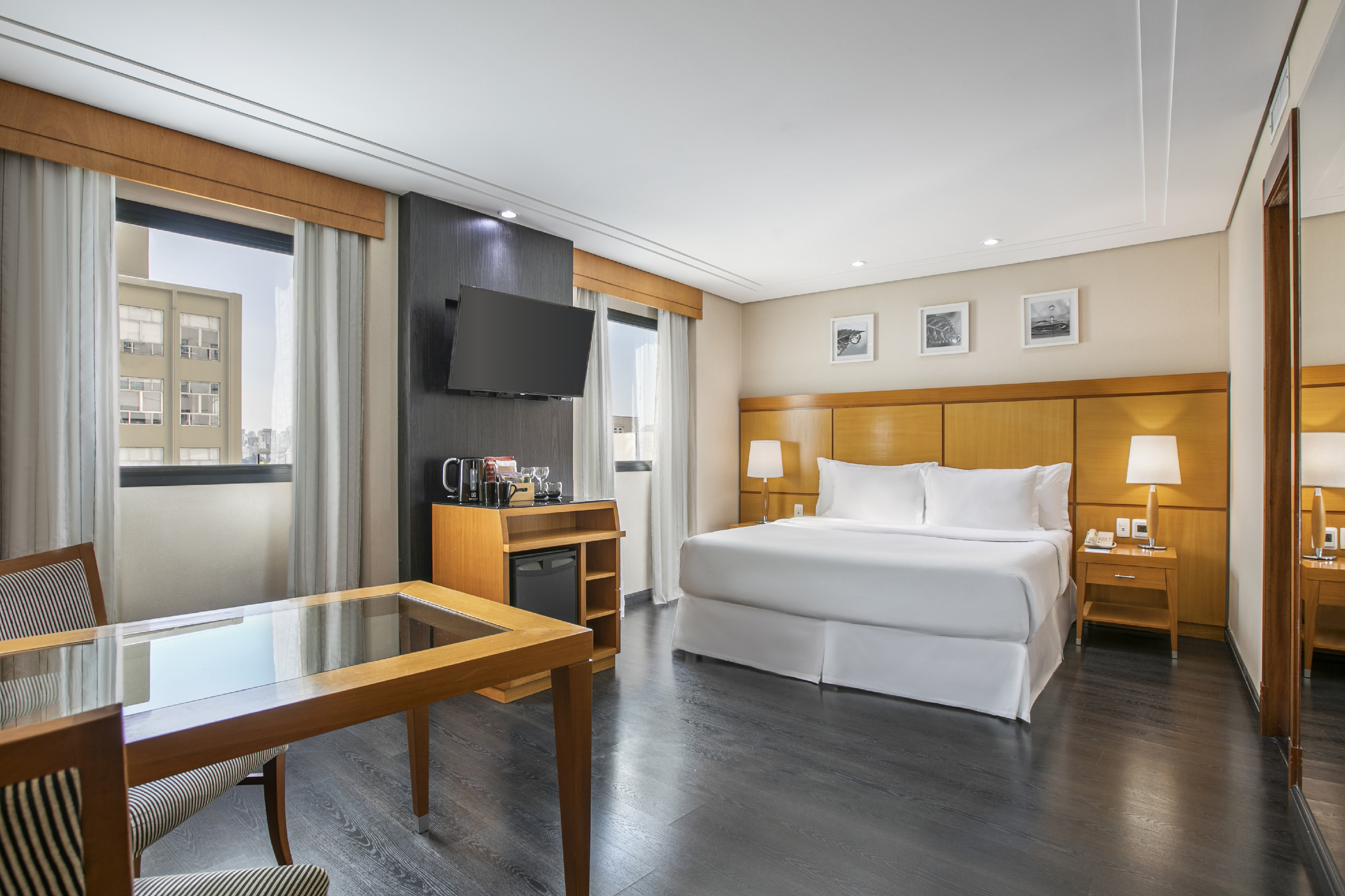 Modern hotel room with king bed, desk, TV, and city view.
