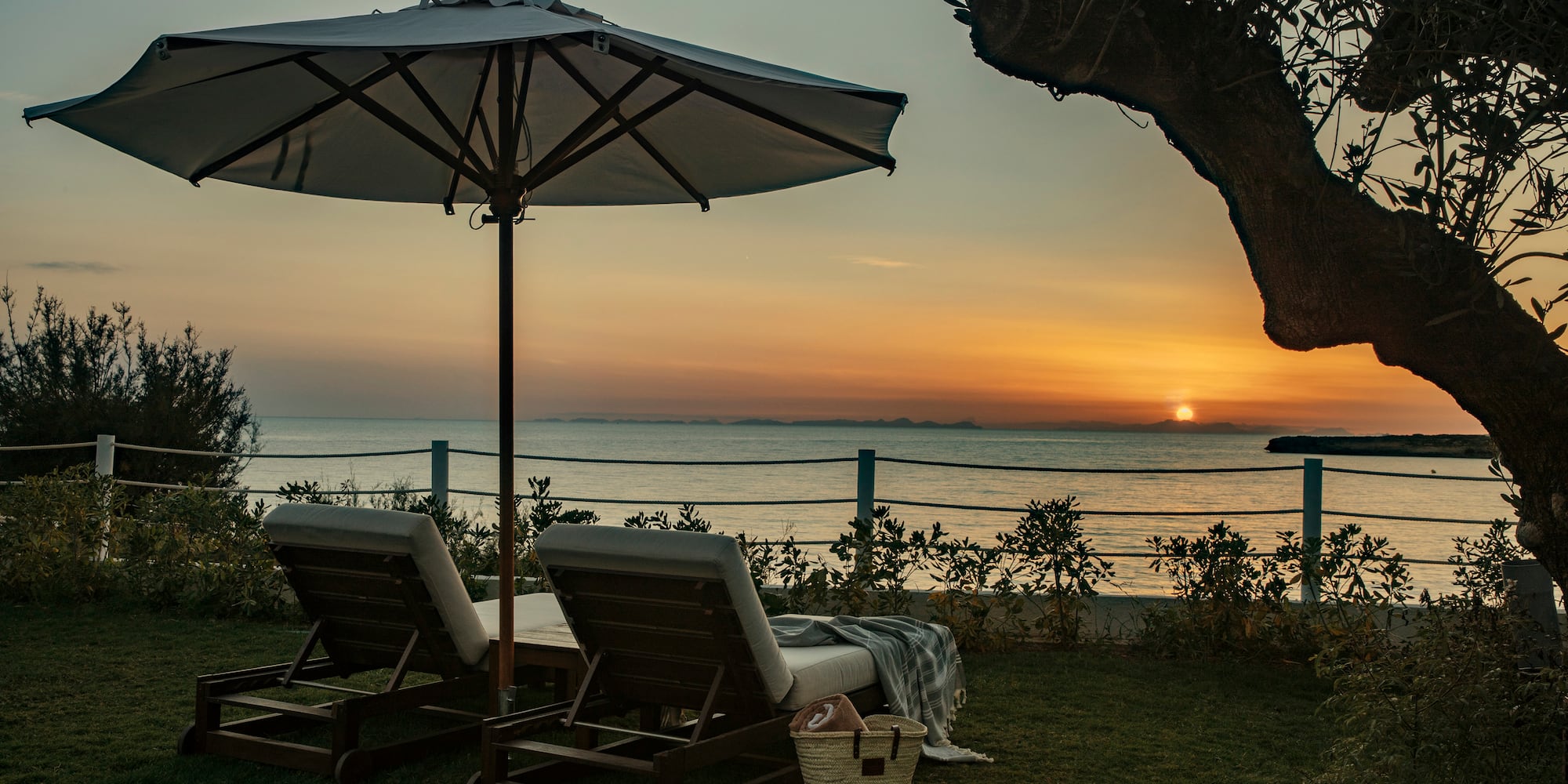 a beach chairs and umbrella on grass by a body of water