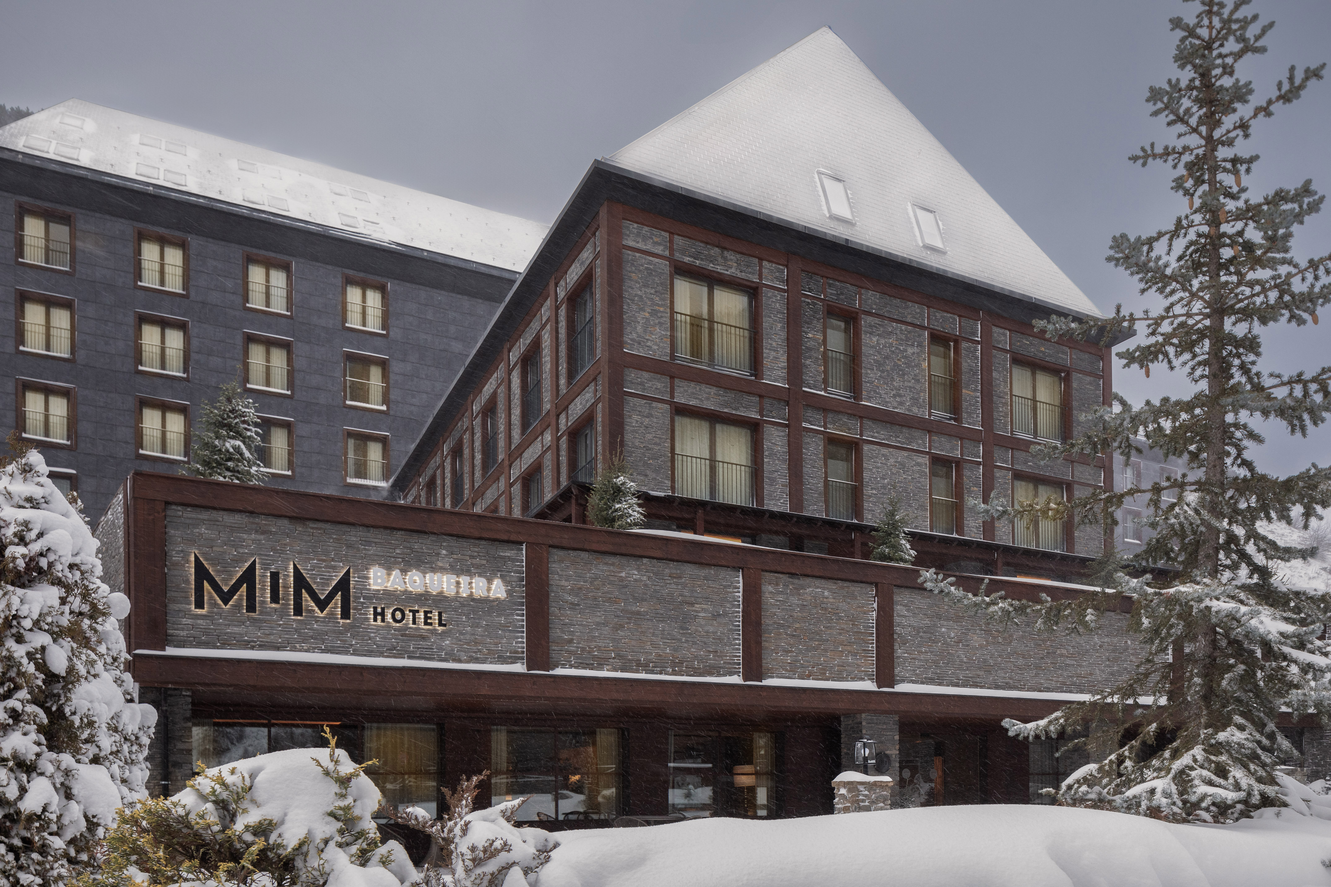 Snowy MiM Baqueira Hotel, modern stone and wood ski resort building in winter.