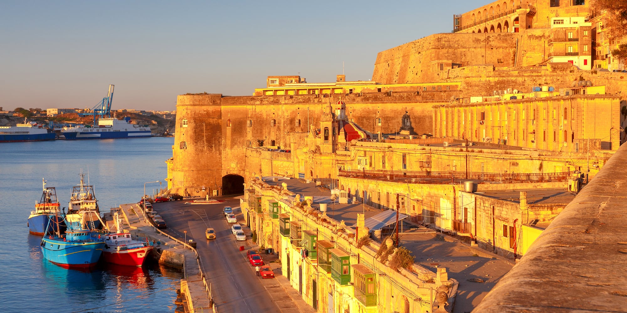 Valletta, Malta harbor at golden hour with historic fortifications and boats.