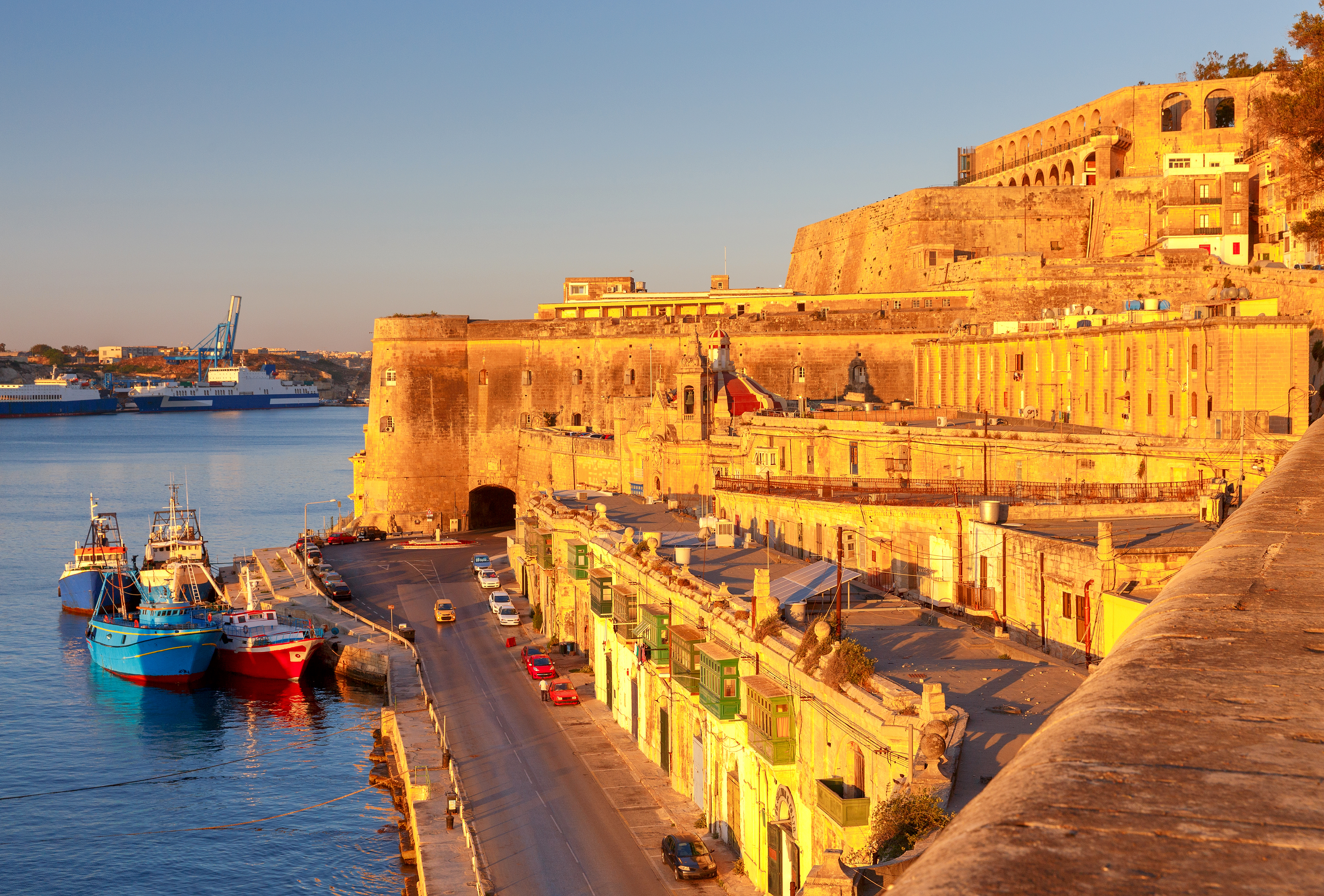Valletta, Malta harbor at golden hour with historic fortifications and boats.
