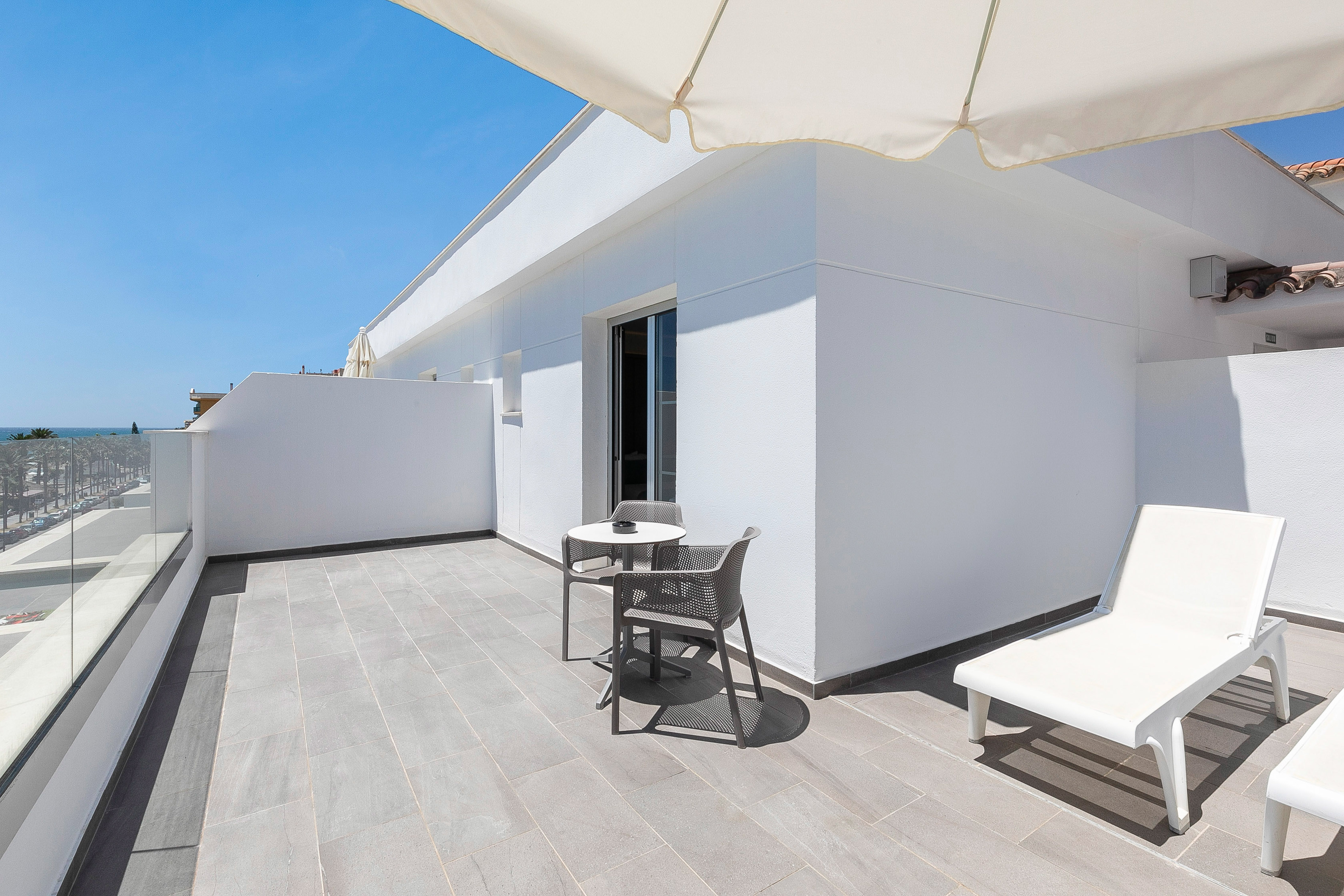 Bright modern terrace with ocean view, outdoor seating, and white sun loungers.