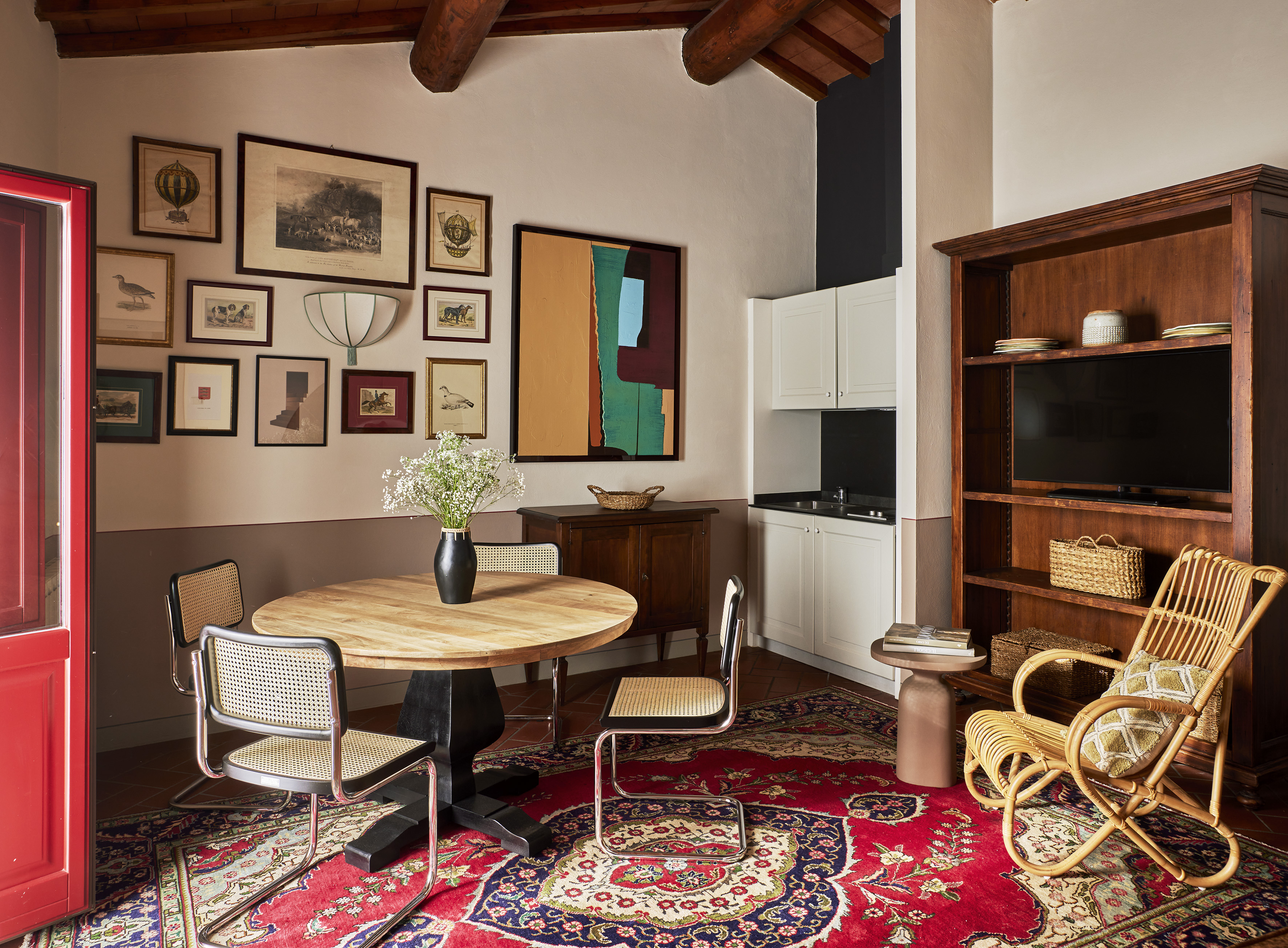 Eclectic living room with dining area, gallery wall, red rug, and kitchenette.