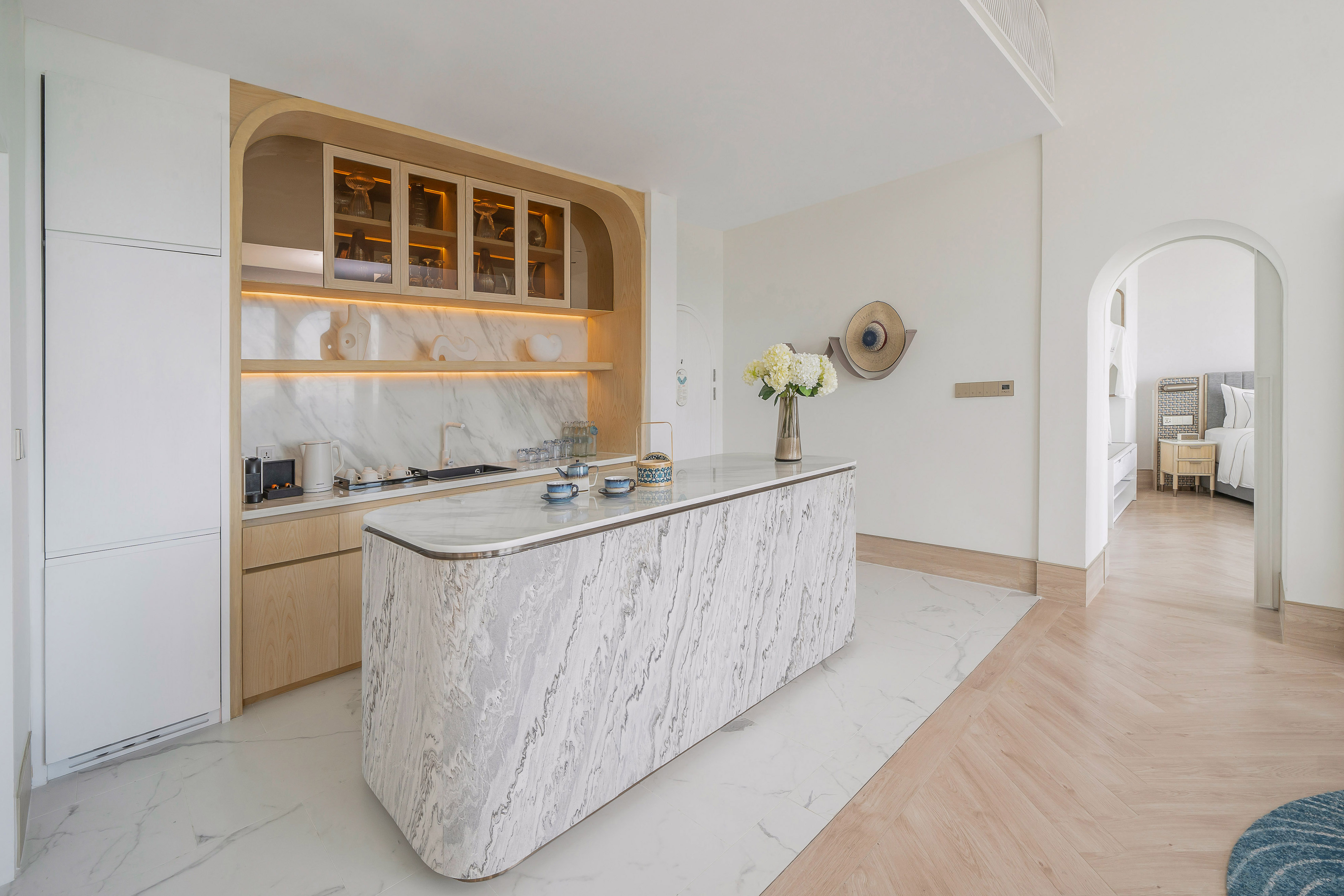 Contemporary kitchen with marble island, light wood cabinets, and an archway.