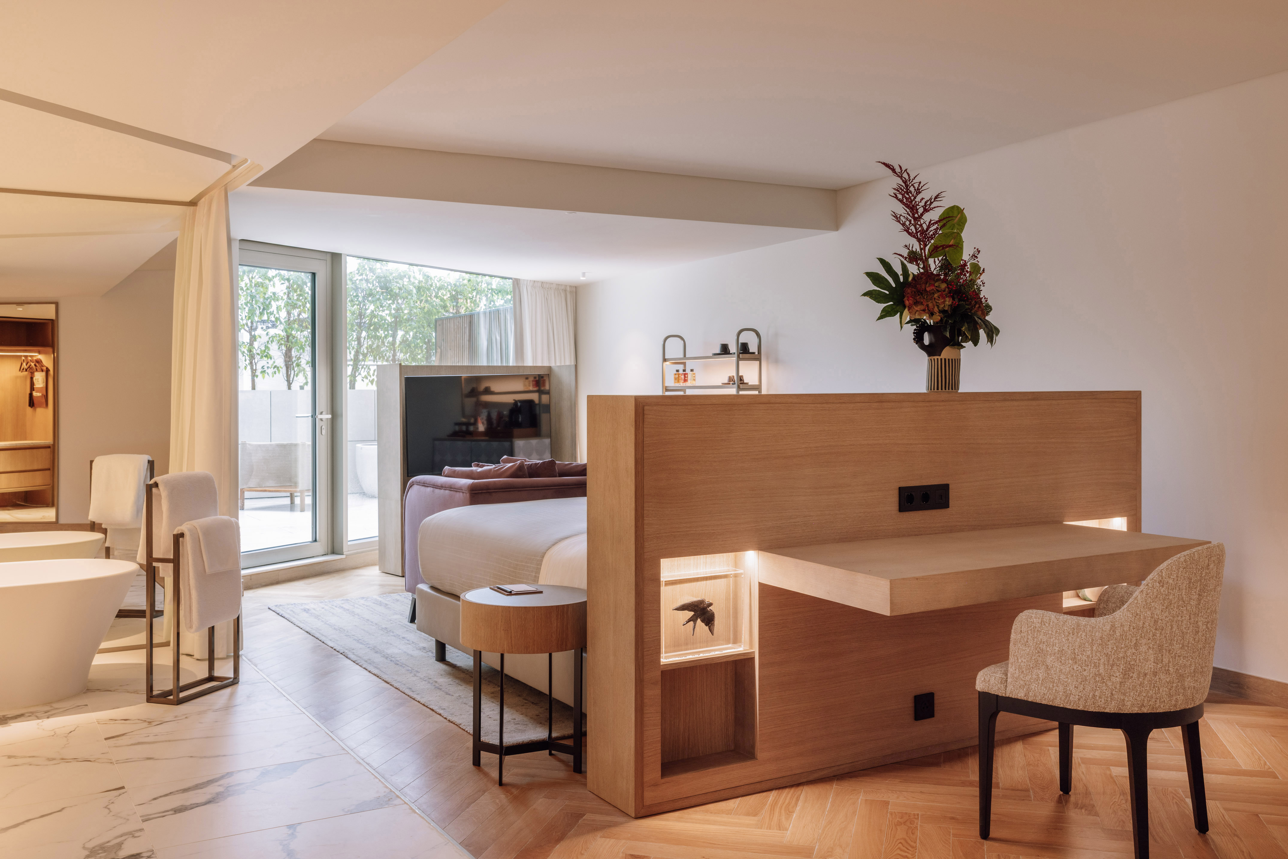 Contemporary hotel suite: king bed, integrated wooden desk, and modern bathtub.