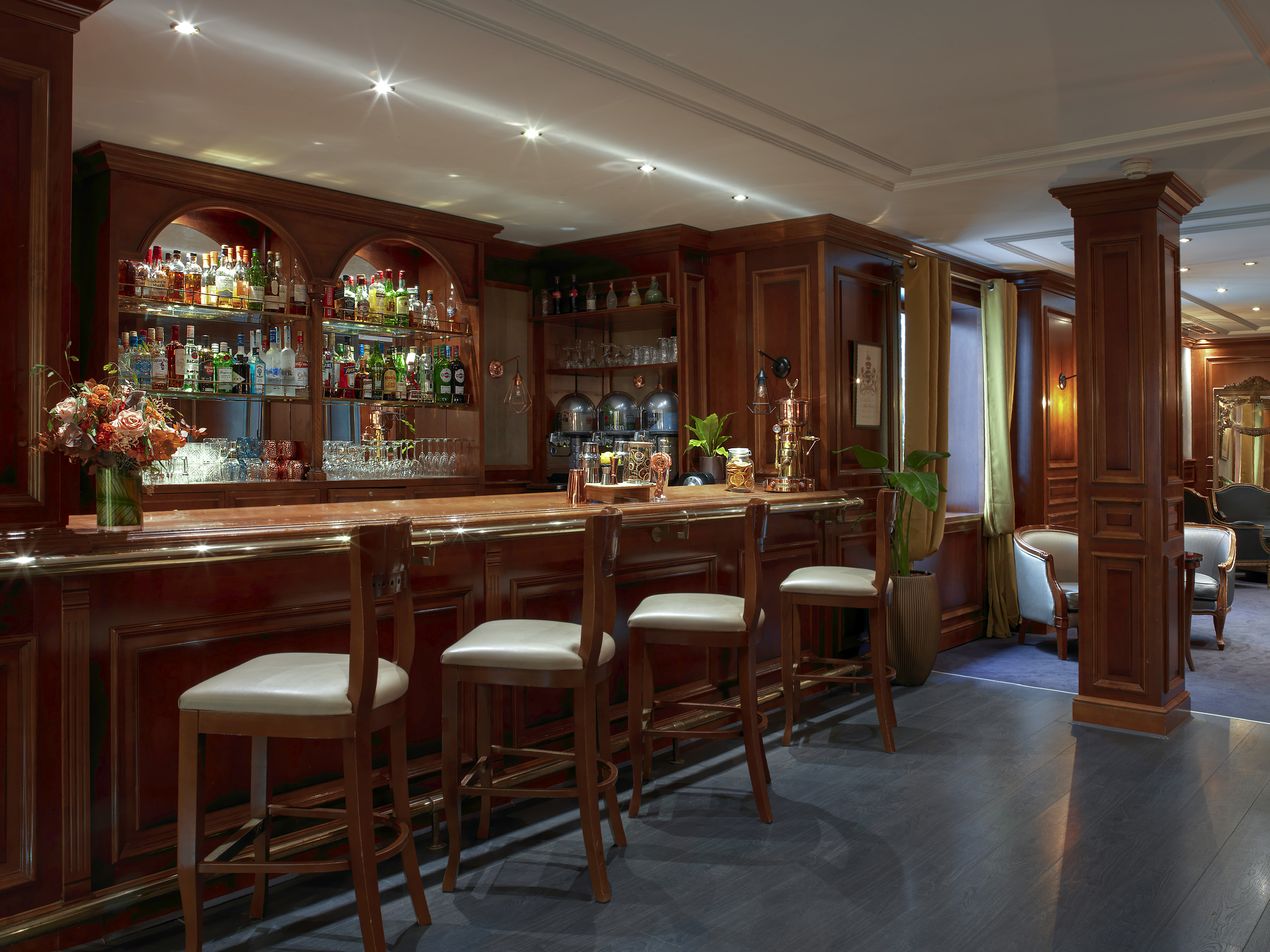 Elegant wooden hotel bar with full liquor display and three bar stools.