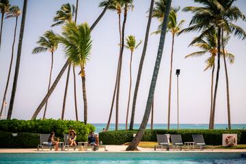 people sitting on lounge chairs by a pool with palm trees