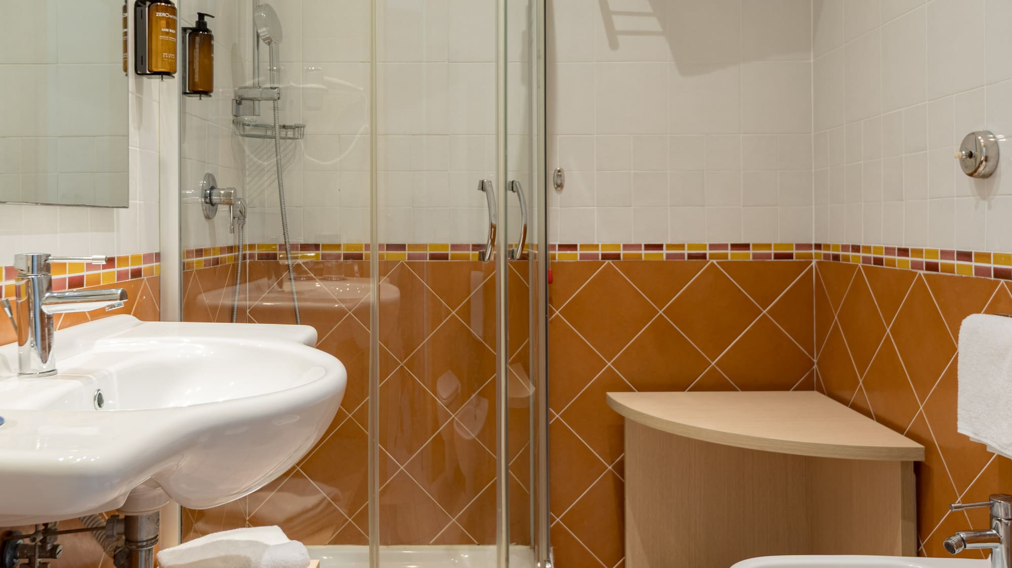 Modern bathroom with glass shower, sink, toilet, bidet, and terracotta tiled walls.