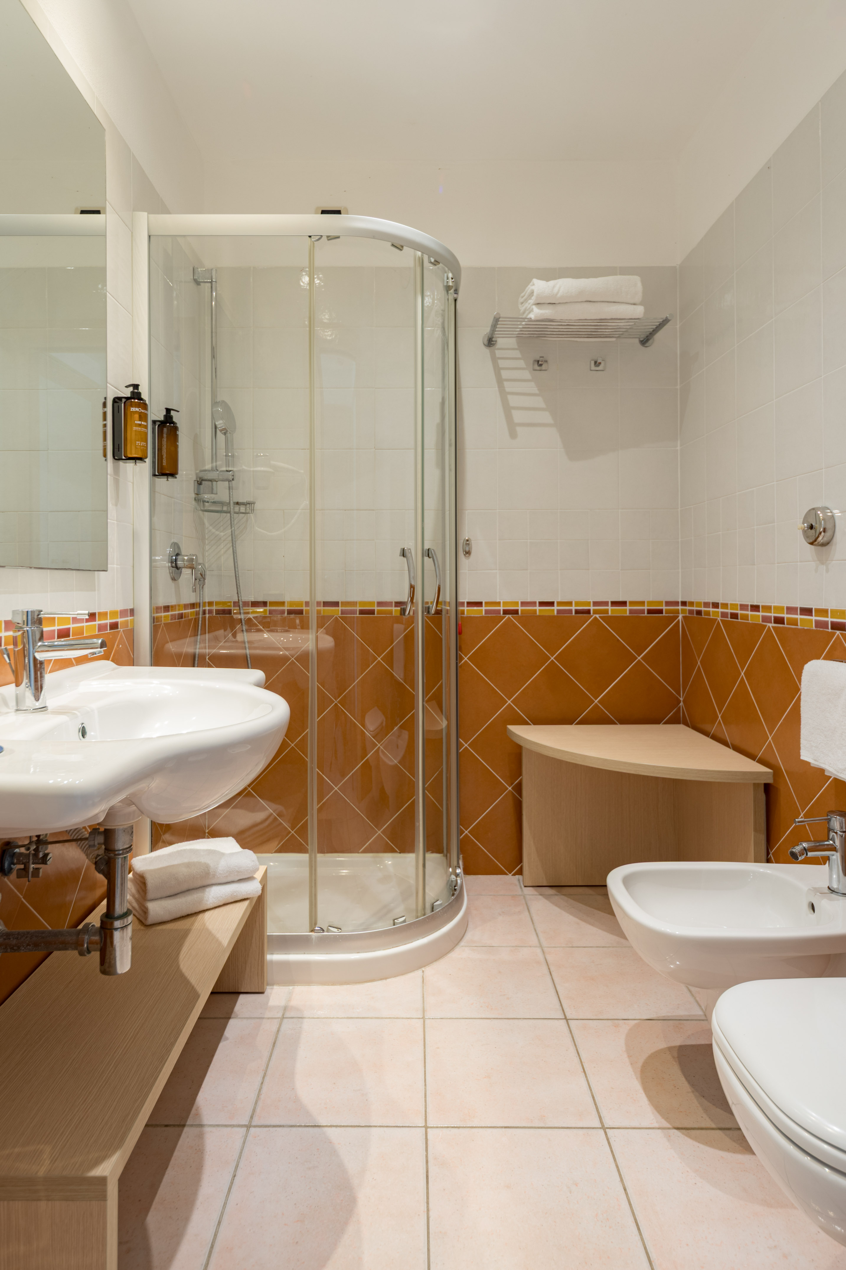 Modern bathroom with glass shower, sink, toilet, bidet, and terracotta tiled walls.