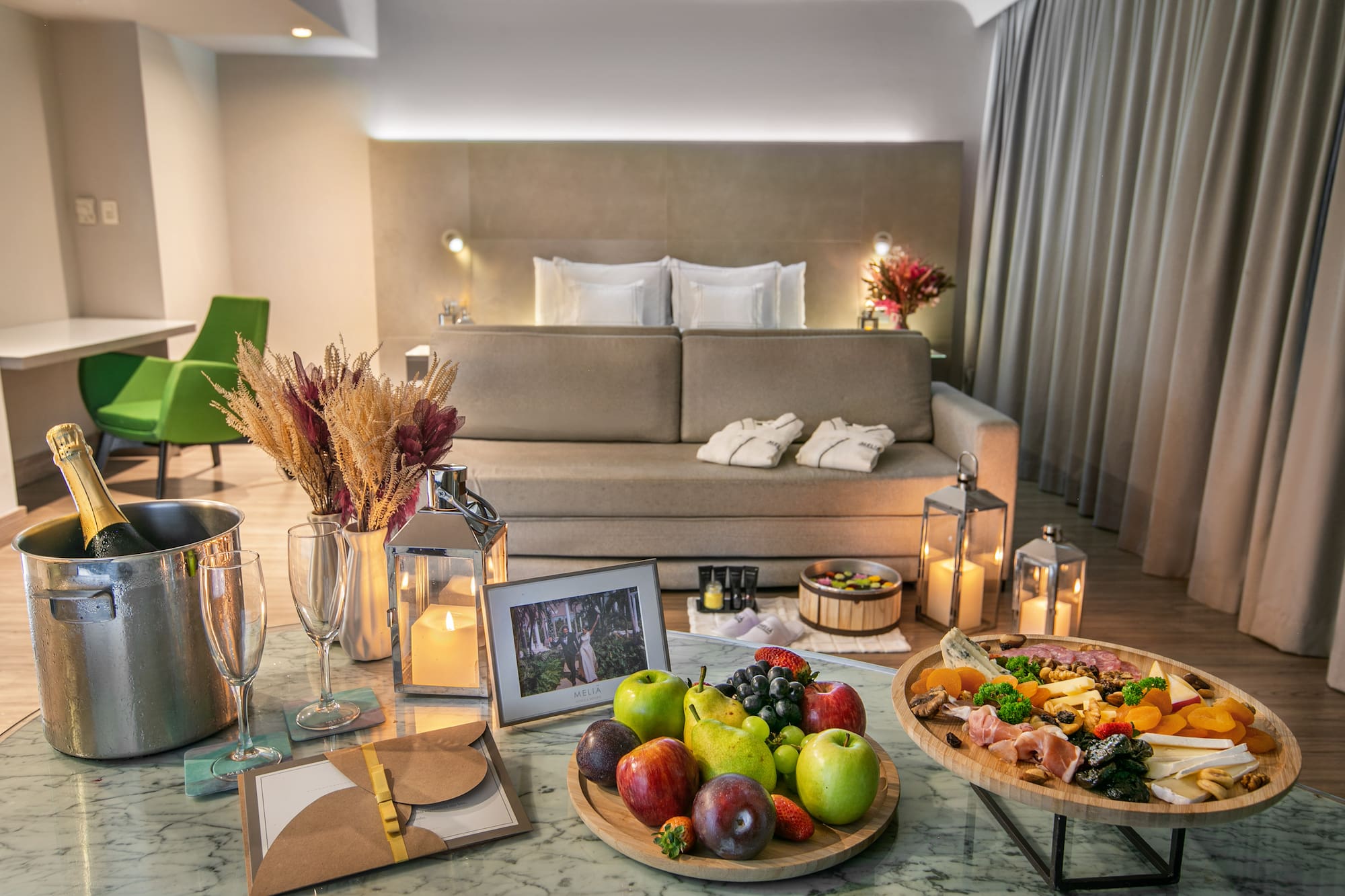 Luxury hotel room with charcuterie board, fruit platter, champagne, and spa bath.