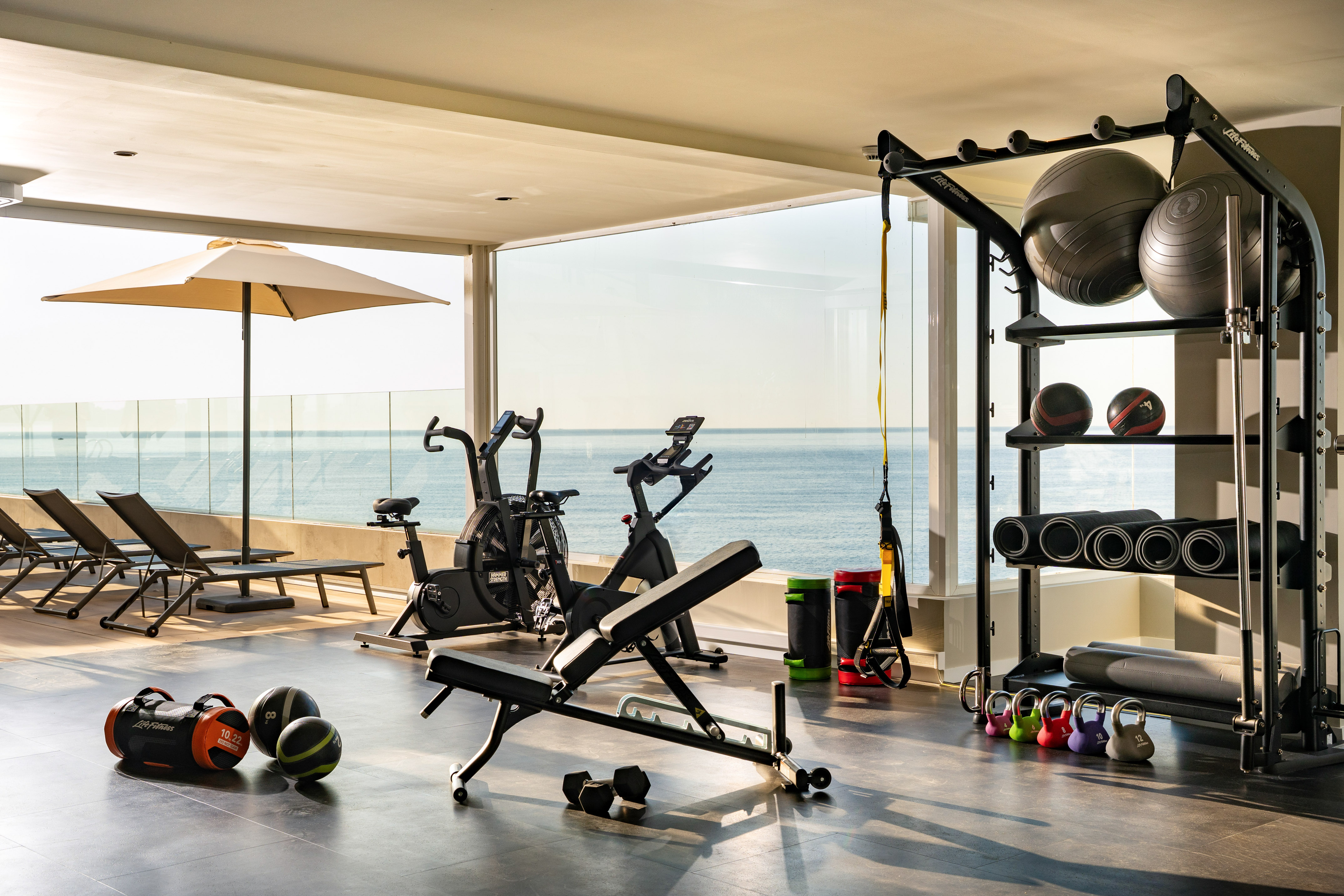 Ocean view fitness center with exercise bikes, weights, and workout gear.