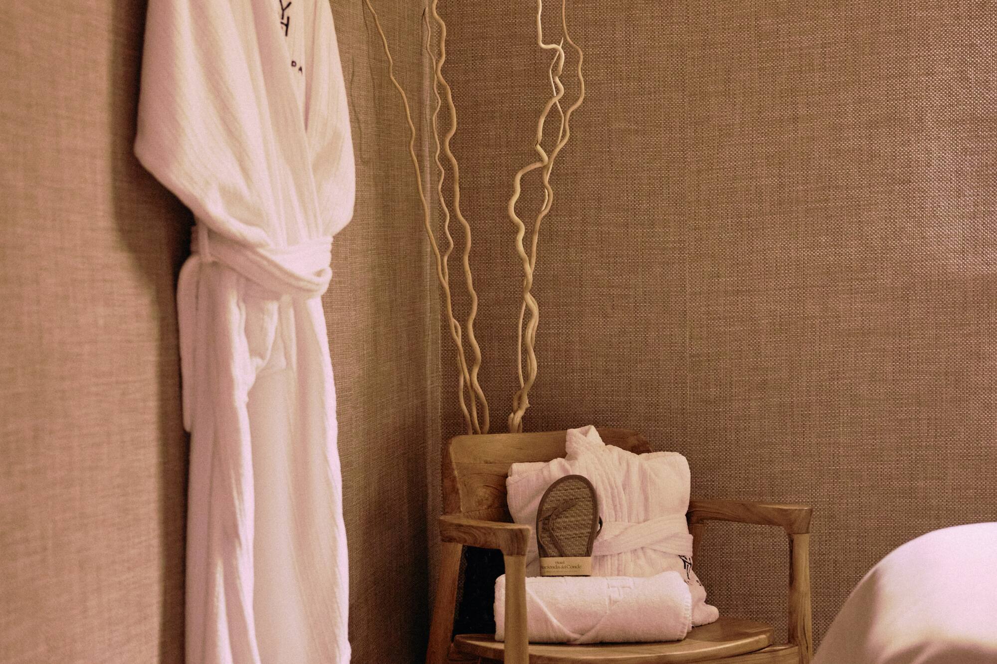 Hotel spa changing area with white bathrobe, folded towels, and wooden chair.