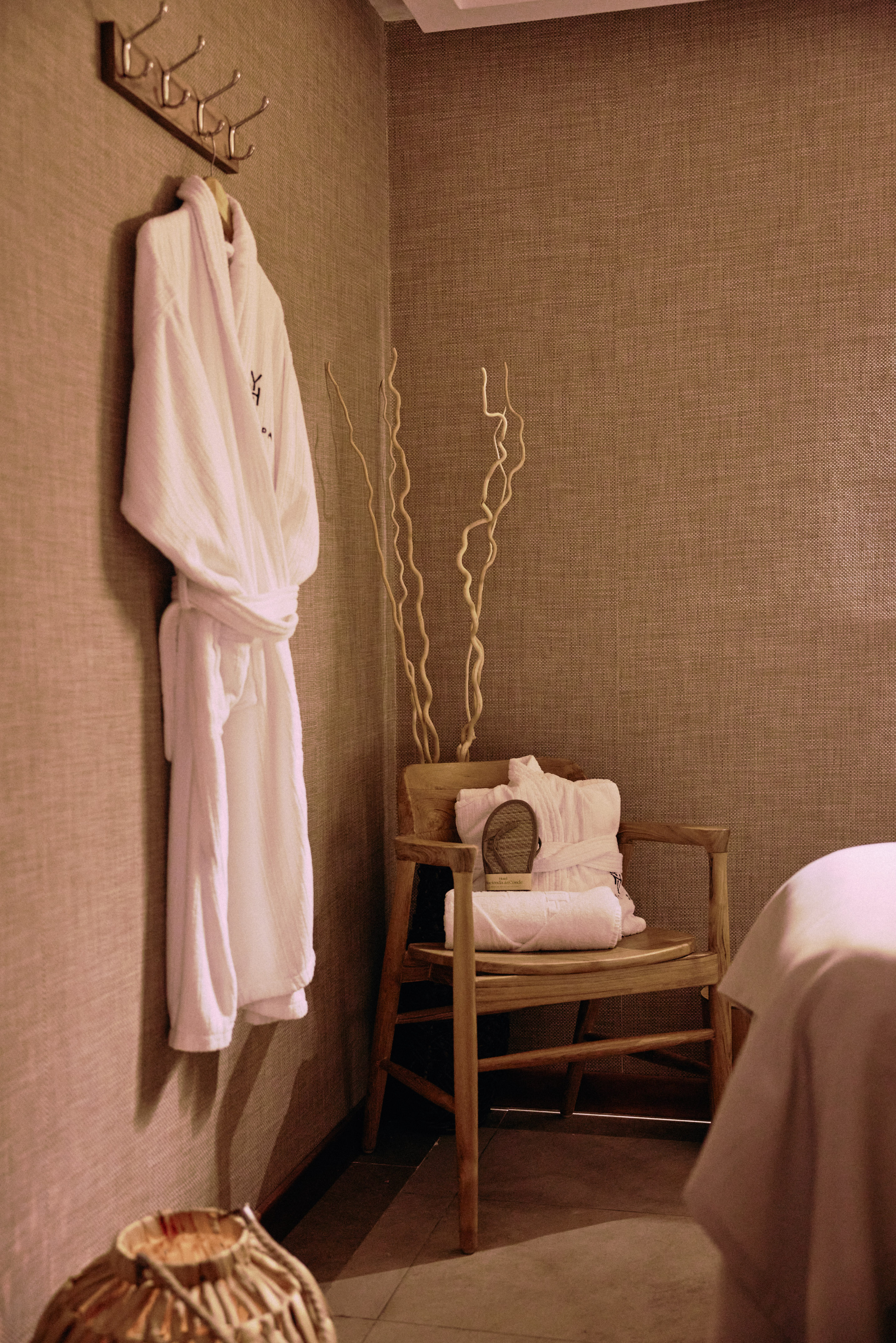 Hotel spa changing area with white bathrobe, folded towels, and wooden chair.