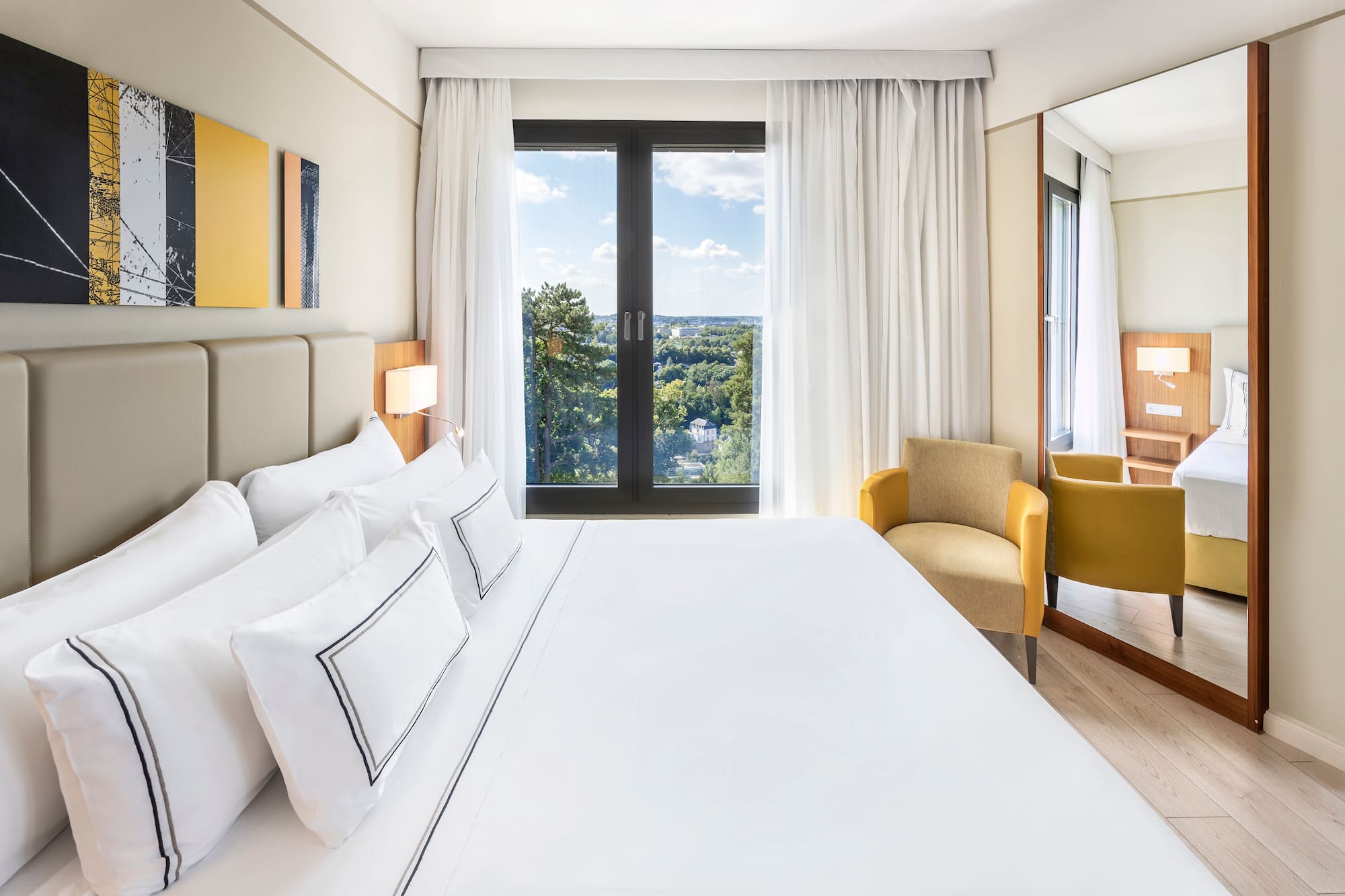 a bed with white sheets and a chair in a room with a view of the city