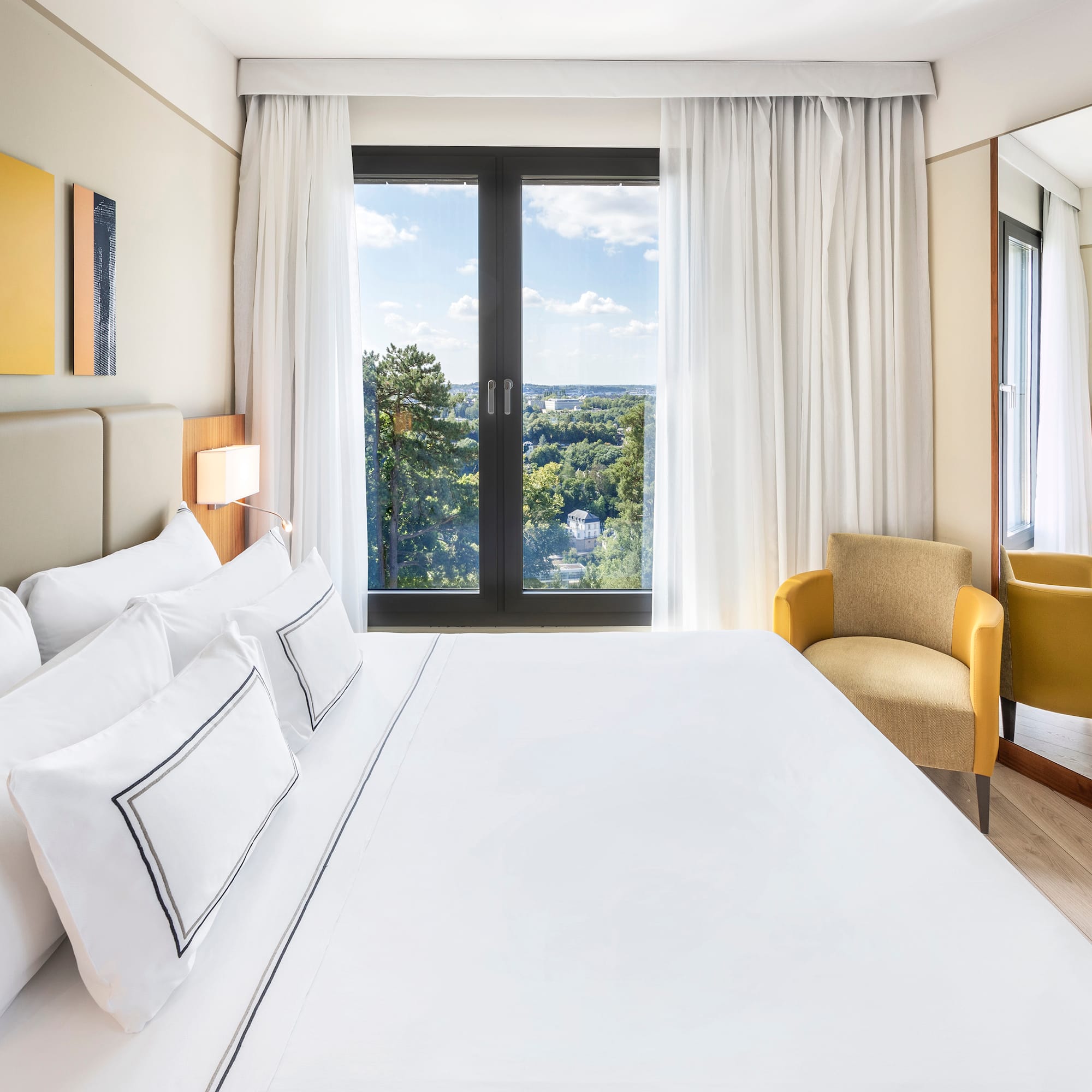 a bed with white sheets and a chair in a room with a view of the city
