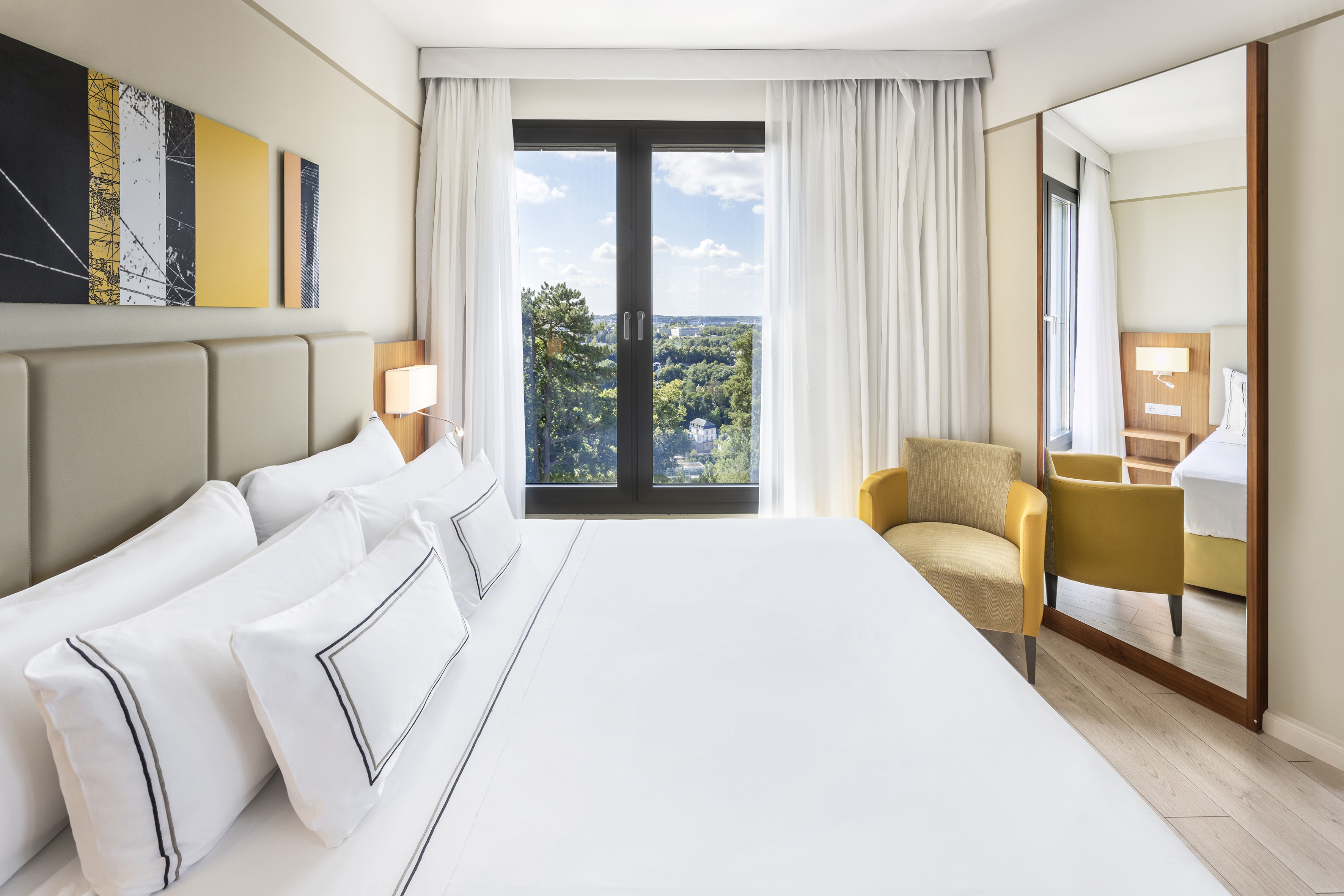 a bed with white sheets and a chair in a room with a view of the city