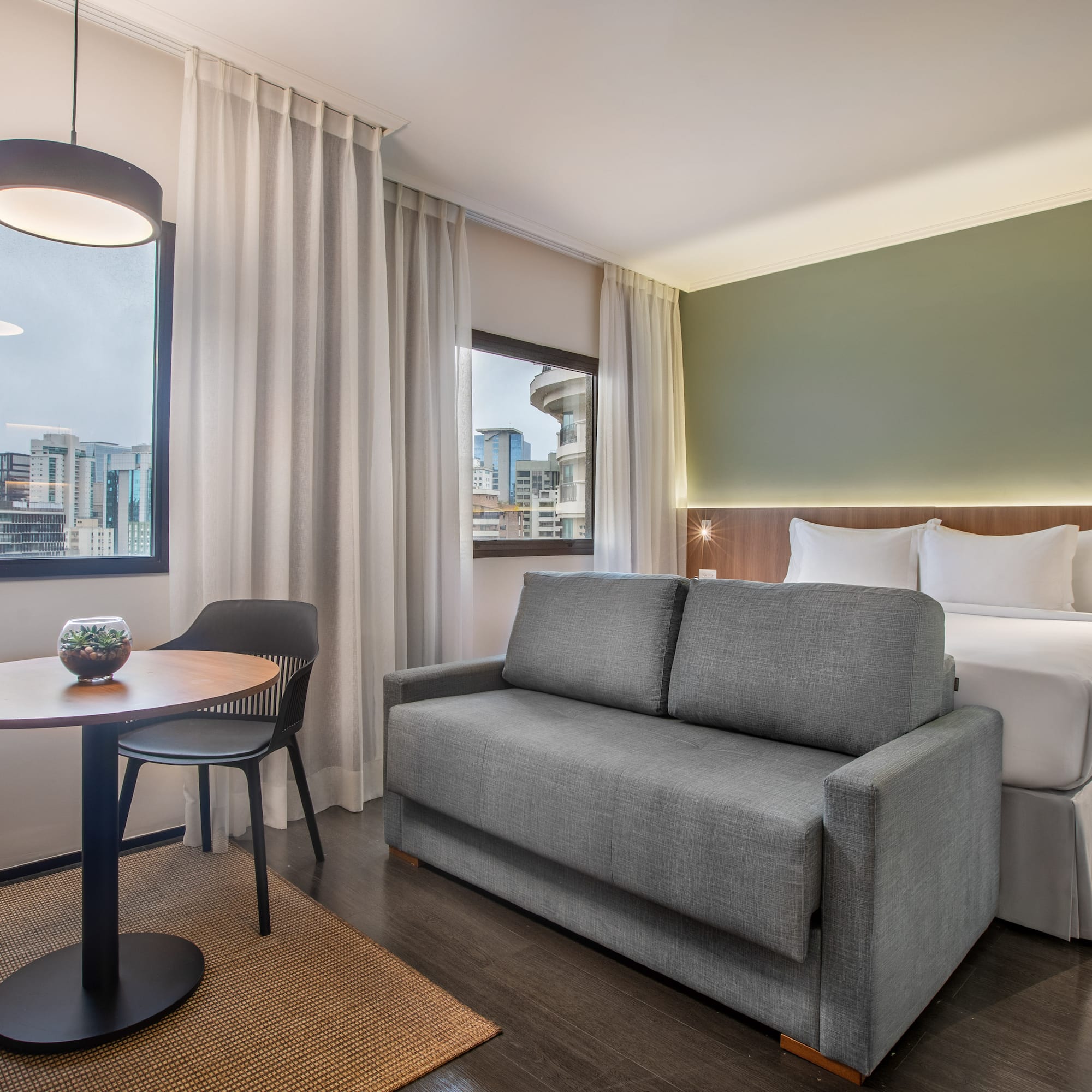 Suite de hotel moderna con cama, sofá, mesa y ventana a la ciudad.