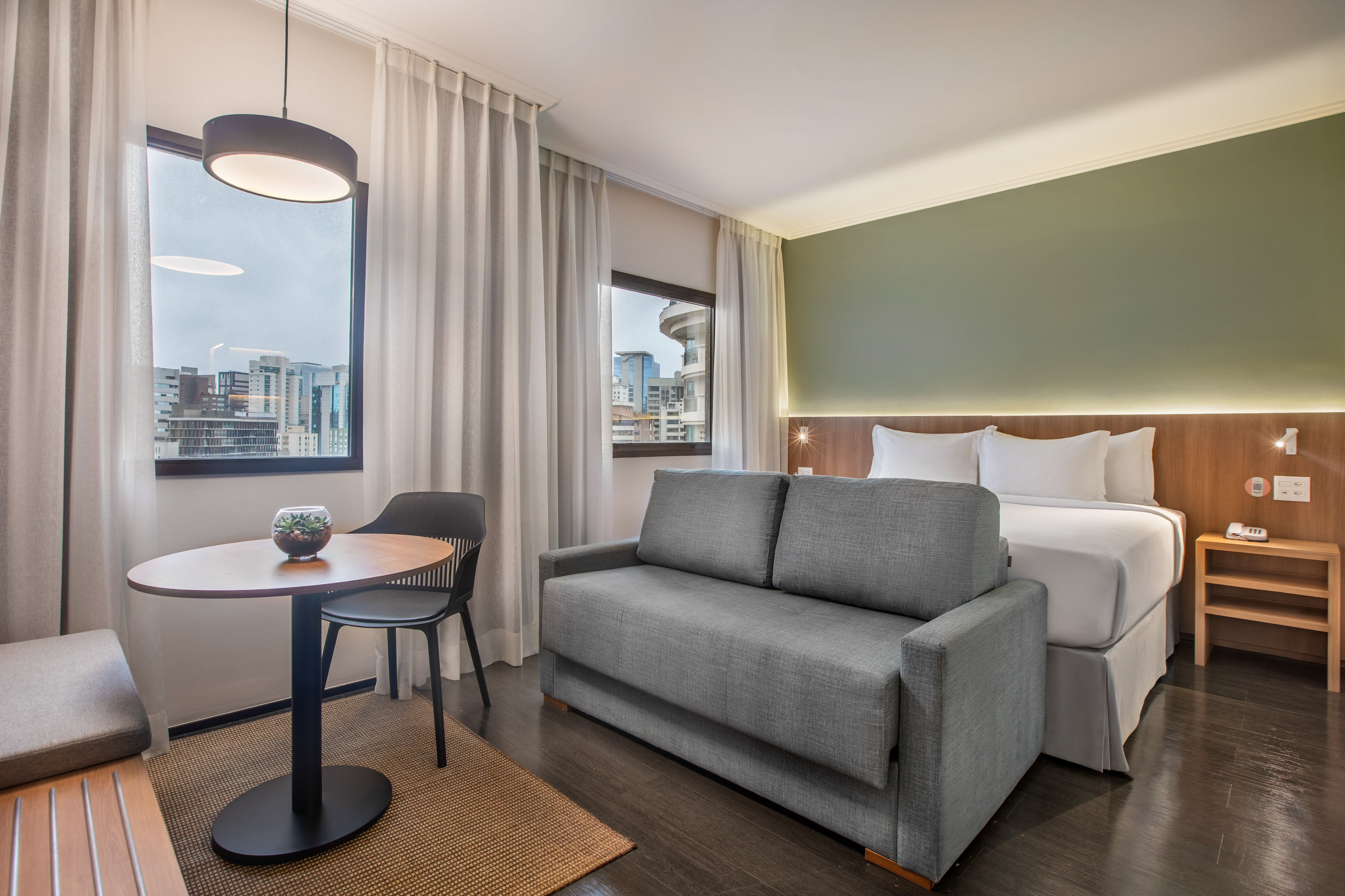 Suite de hotel moderna con cama, sofá, mesa y ventana a la ciudad.