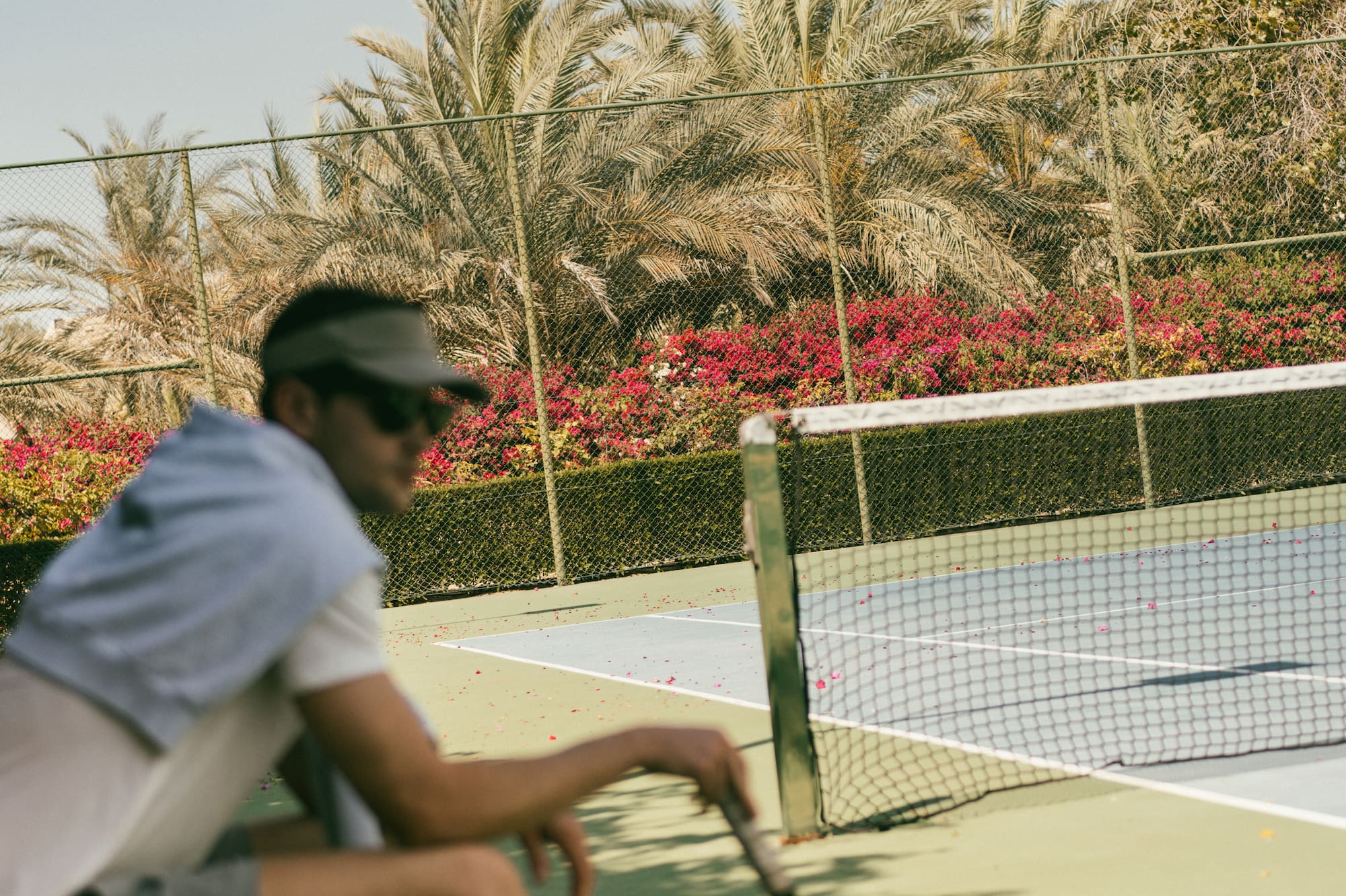 Tennis player with racket resting on court bench under palm trees.