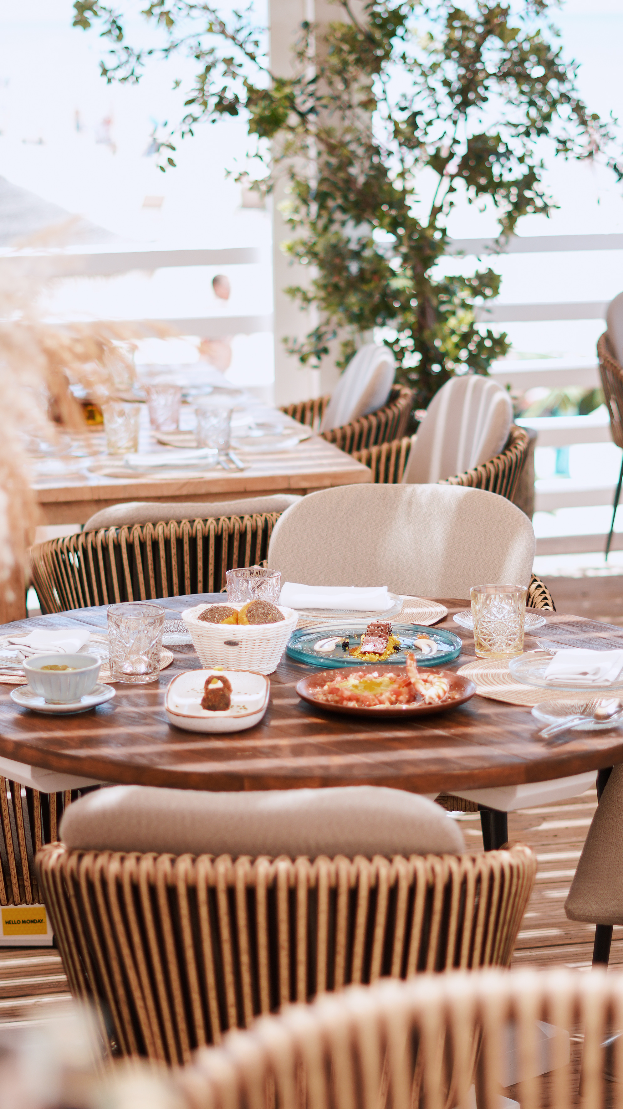 Outdoor dining patio with set wooden tables, wicker chairs, and appetizers.