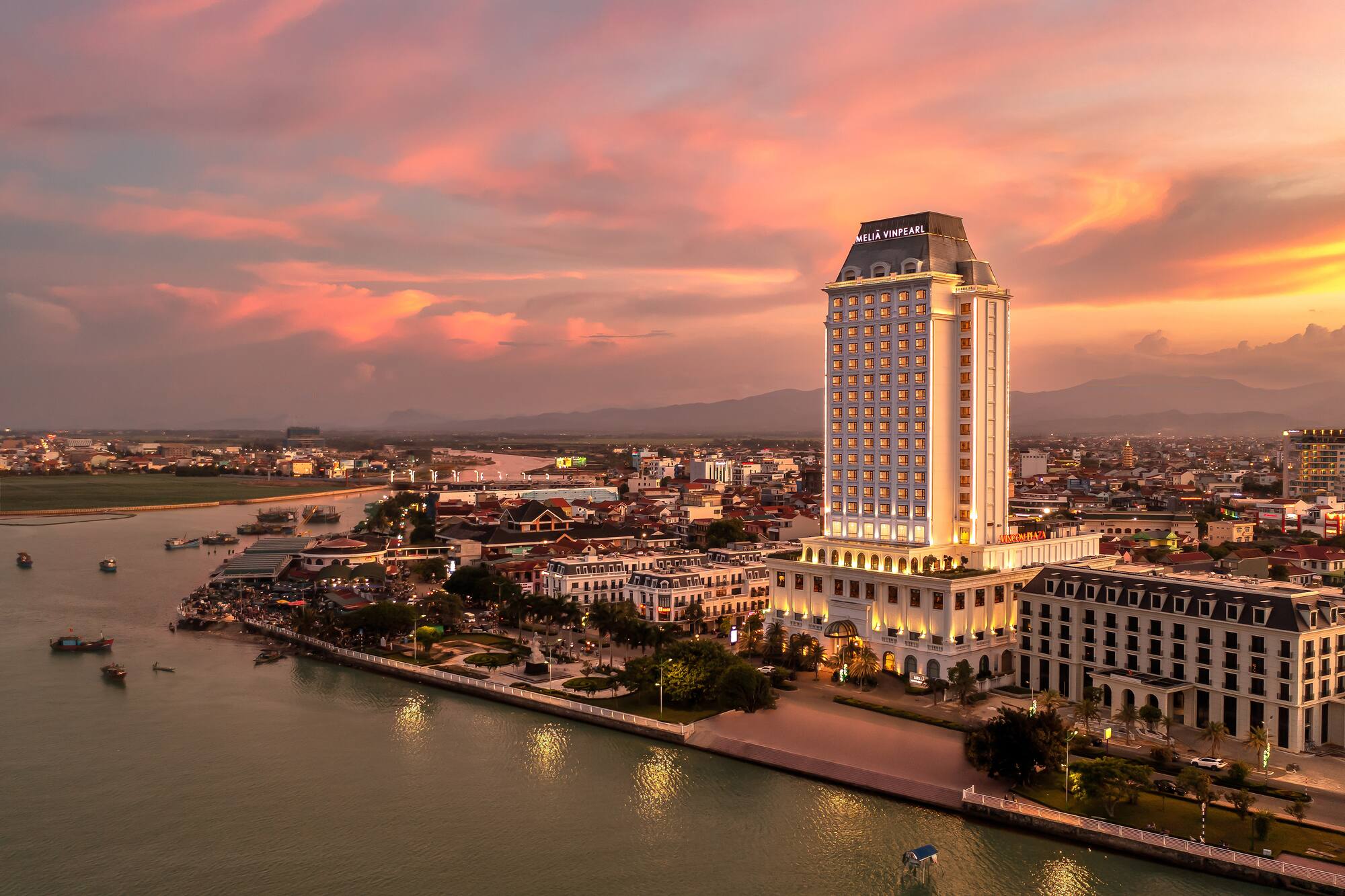 Melia Vinpearl hotel towering over a river city at vibrant sunset.