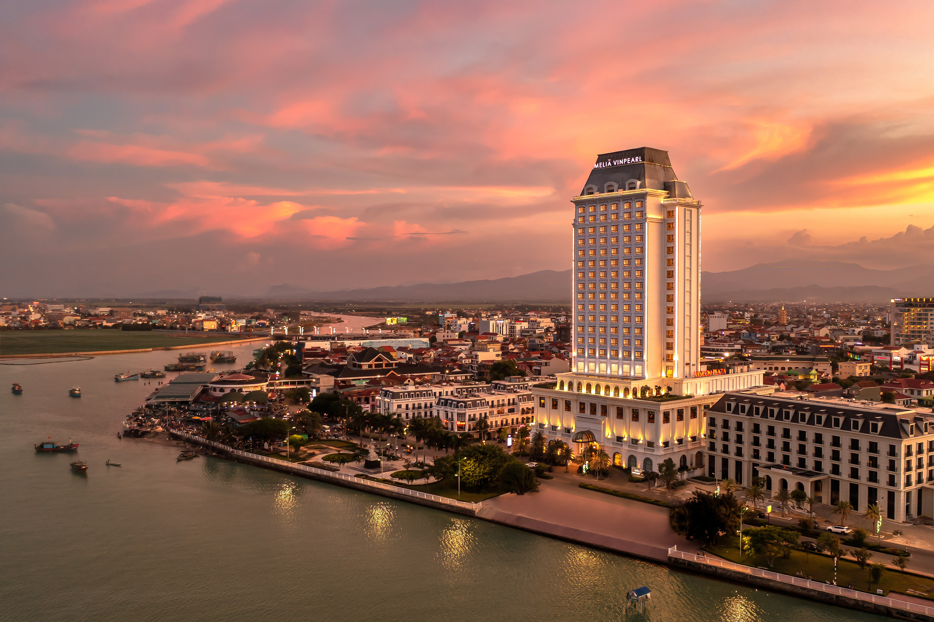 Melia Vinpearl hotel towering over a river city at vibrant sunset.