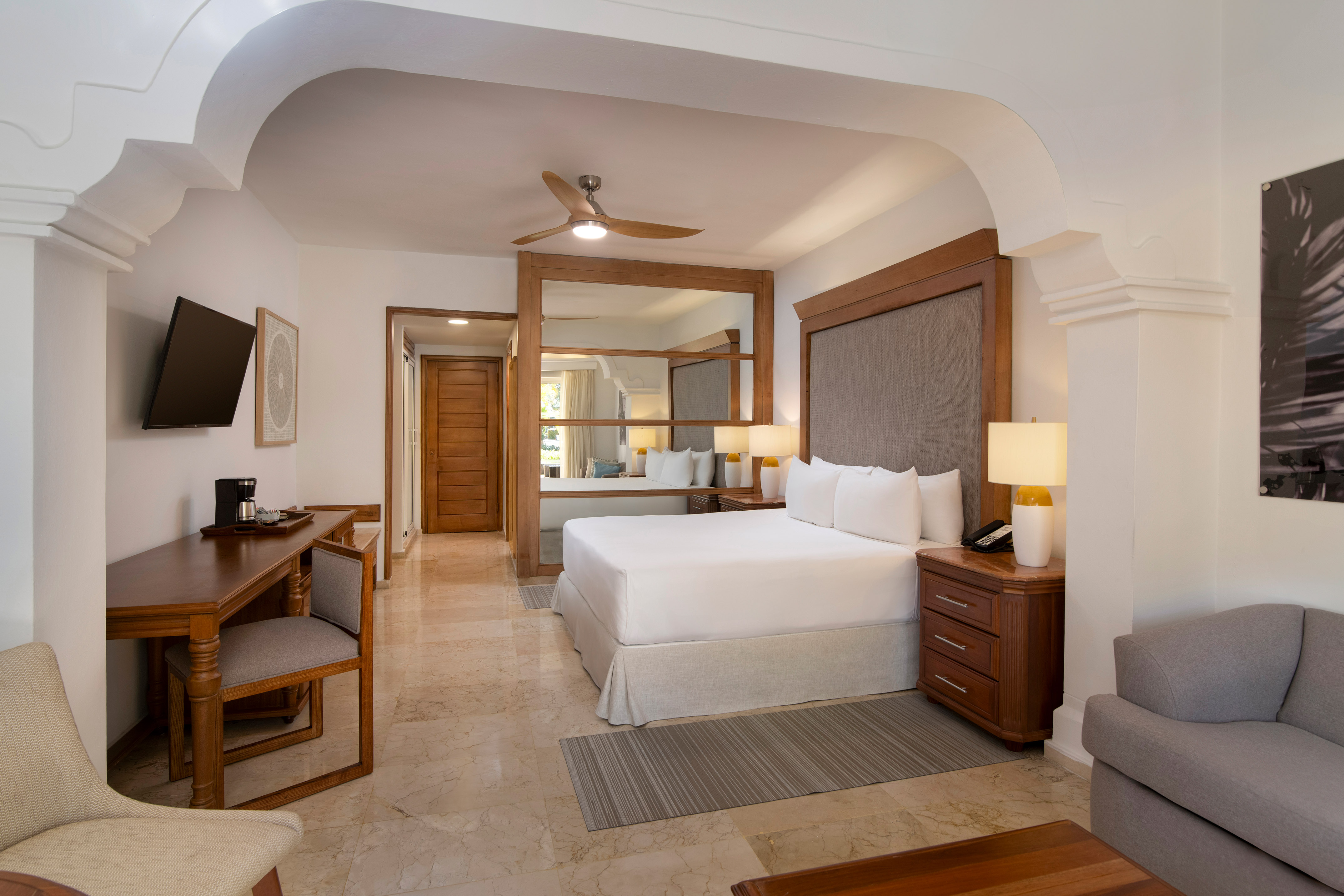Luxurious hotel bedroom with king bed, desk, sitting area, and ceiling fan.