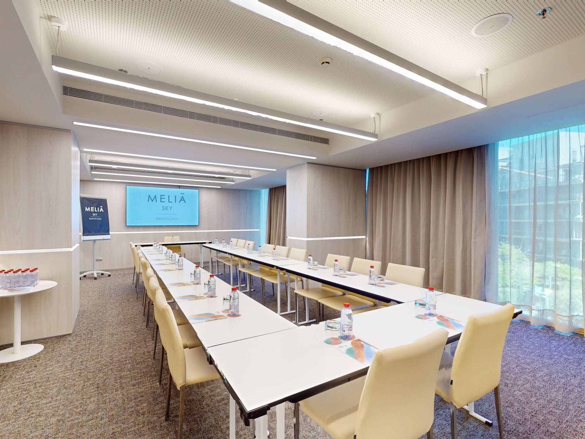 Modern Melià Sky Barcelona meeting room with U-shaped table setup and screen.