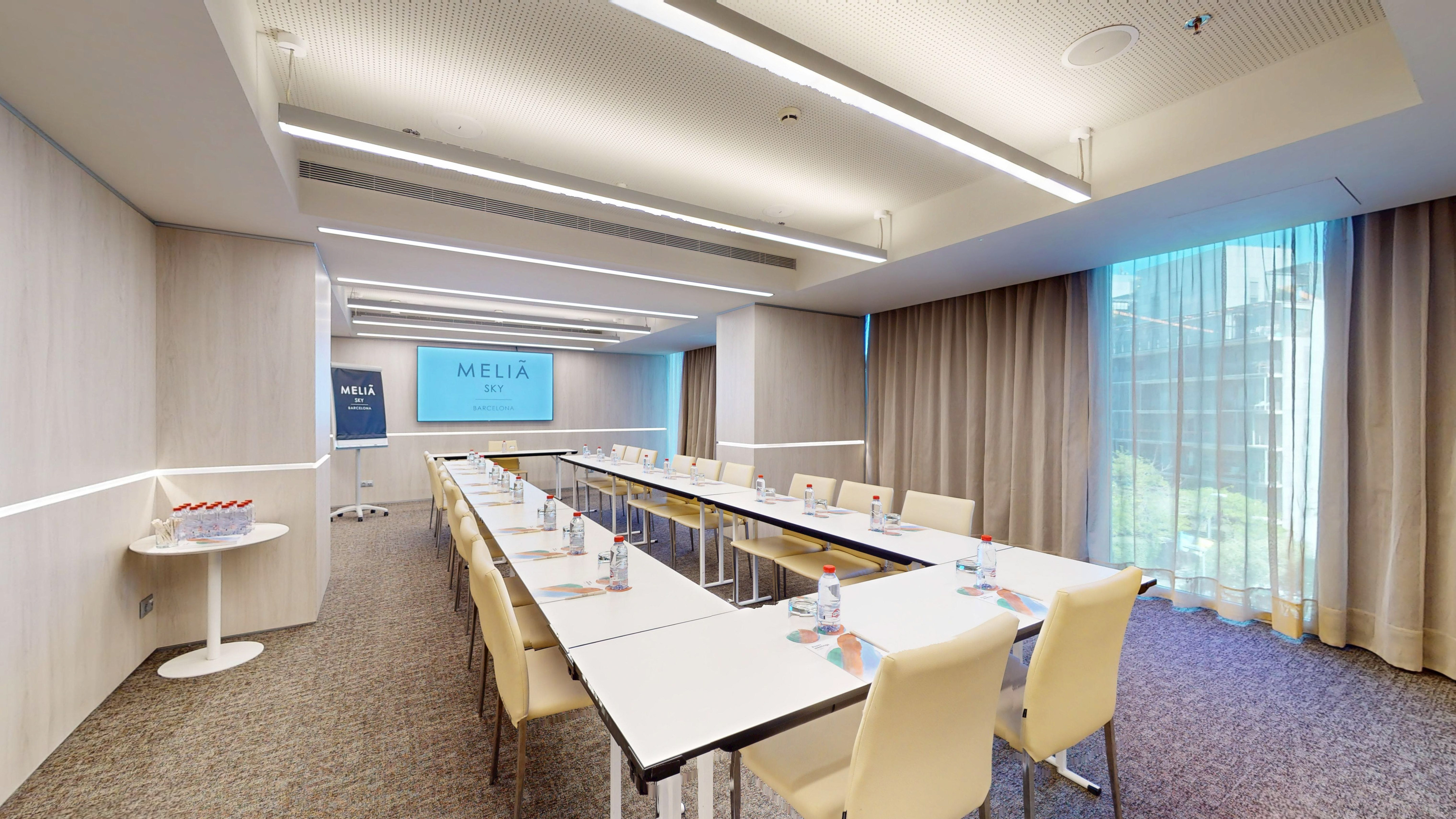 Modern Melià Sky Barcelona meeting room with U-shaped table setup and screen.