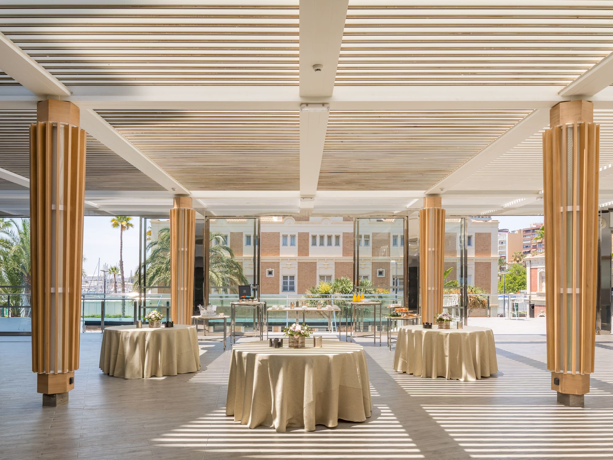 Modern event space with slatted ceiling, tables, and waterfront marina view.